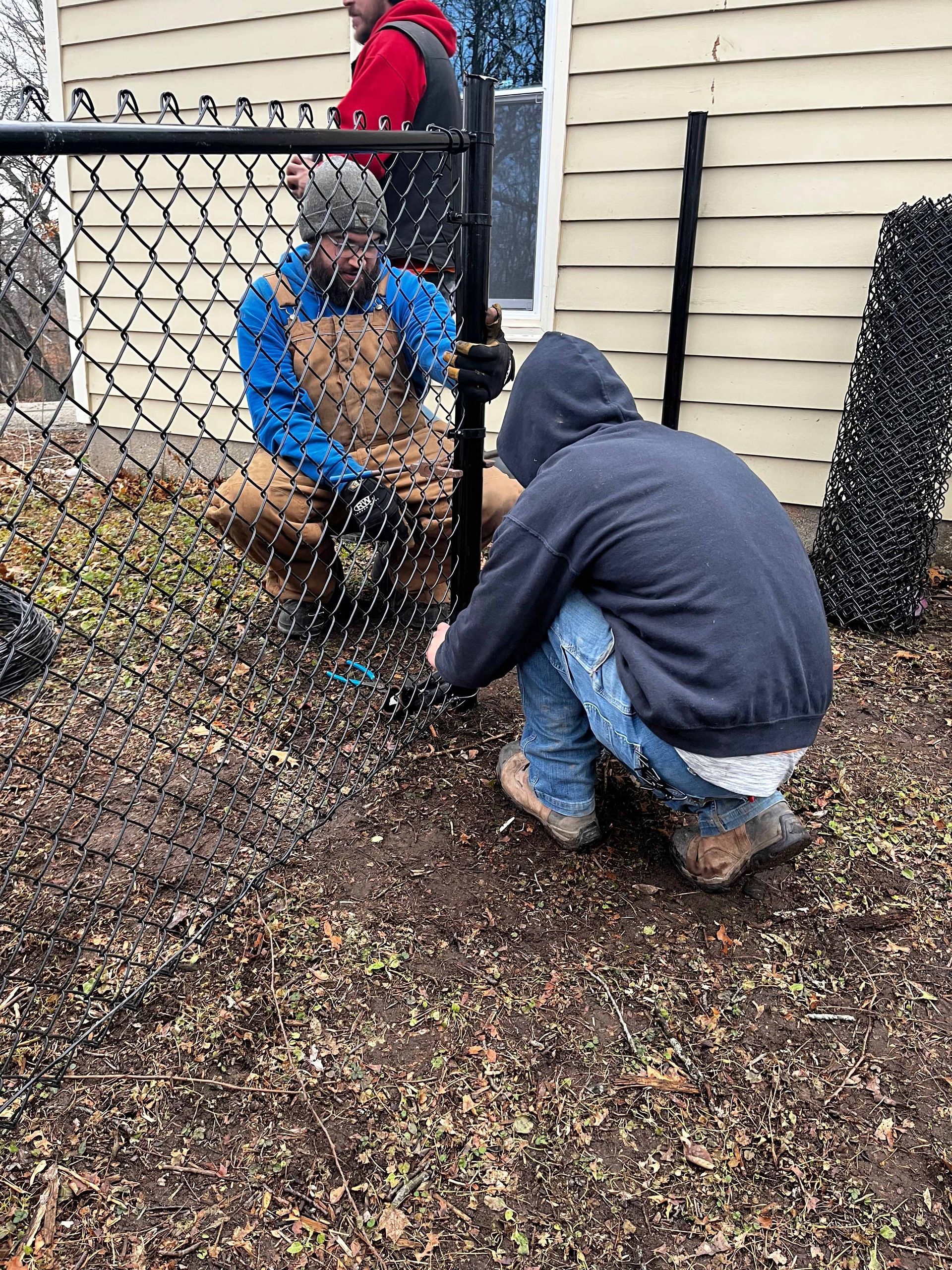 Two men are working on a chain link fence in front of a house.