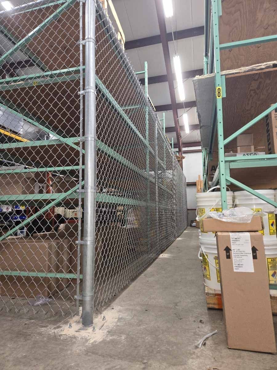 A chain link fence surrounds a warehouse filled with shelves and buckets