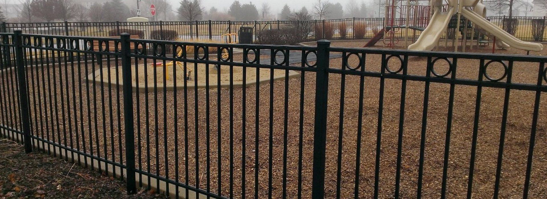 A black metal fence surrounds a playground in a park.