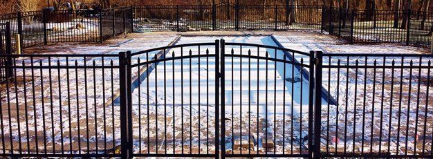 A metal fence surrounds a swimming pool in the snow.