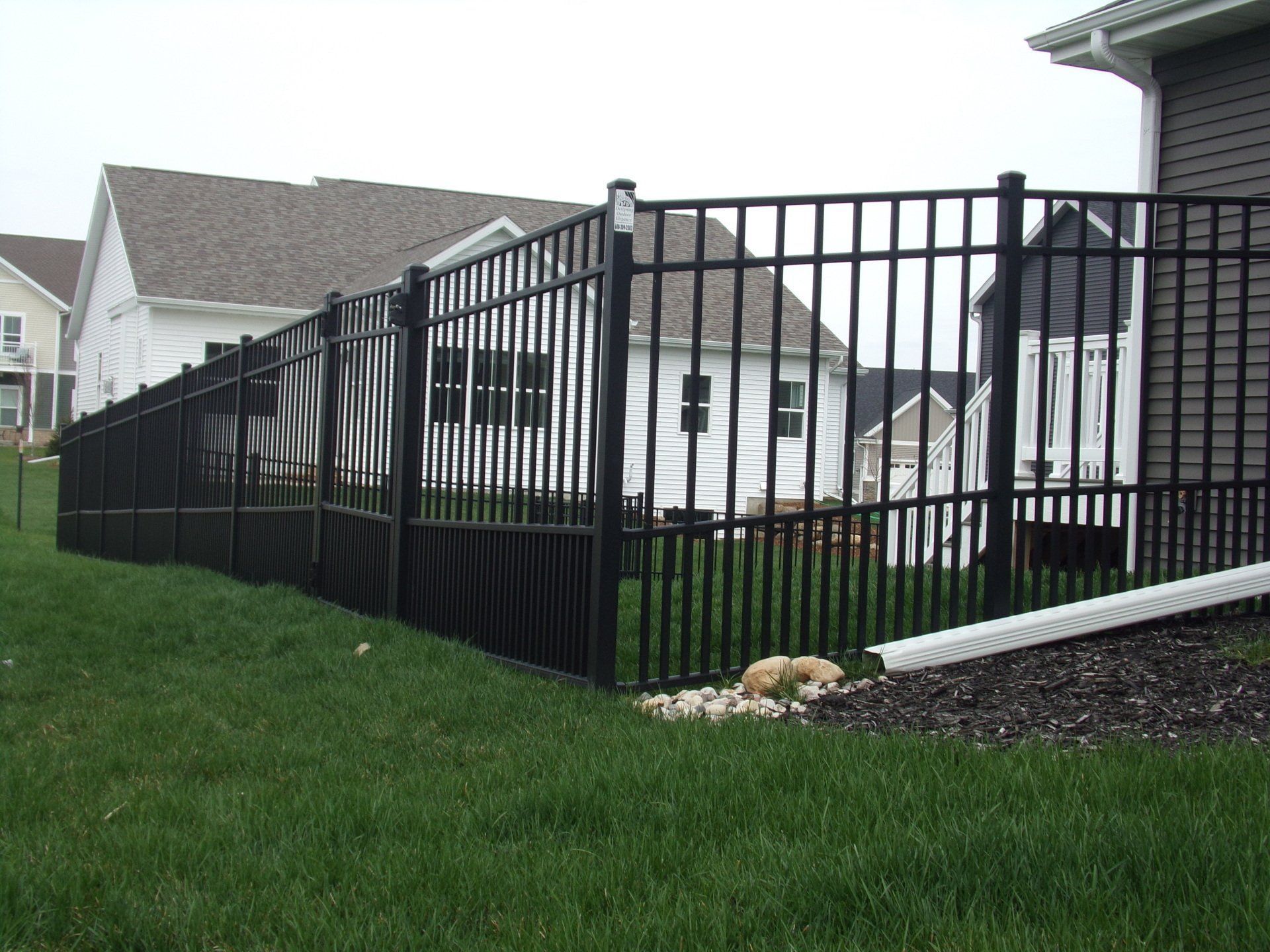 A black fence surrounds a lush green yard in front of a house