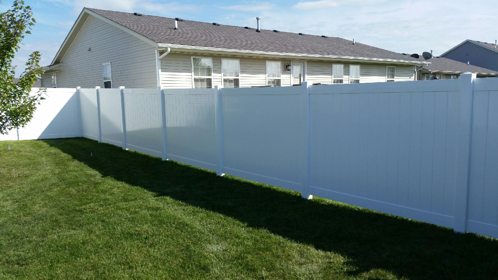 A white fence surrounds a lush green yard in front of a house.