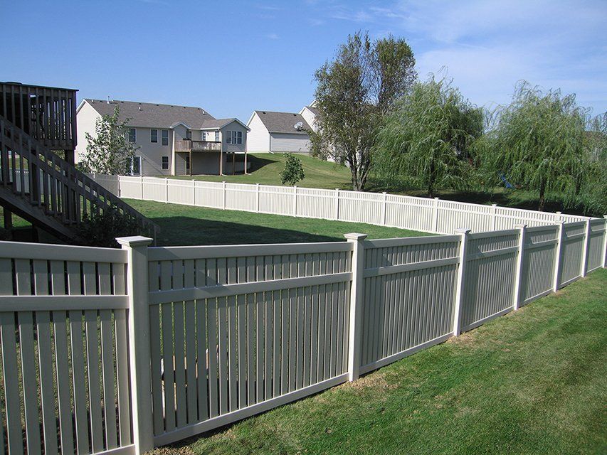 A white fence surrounds a lush green yard with houses in the background.