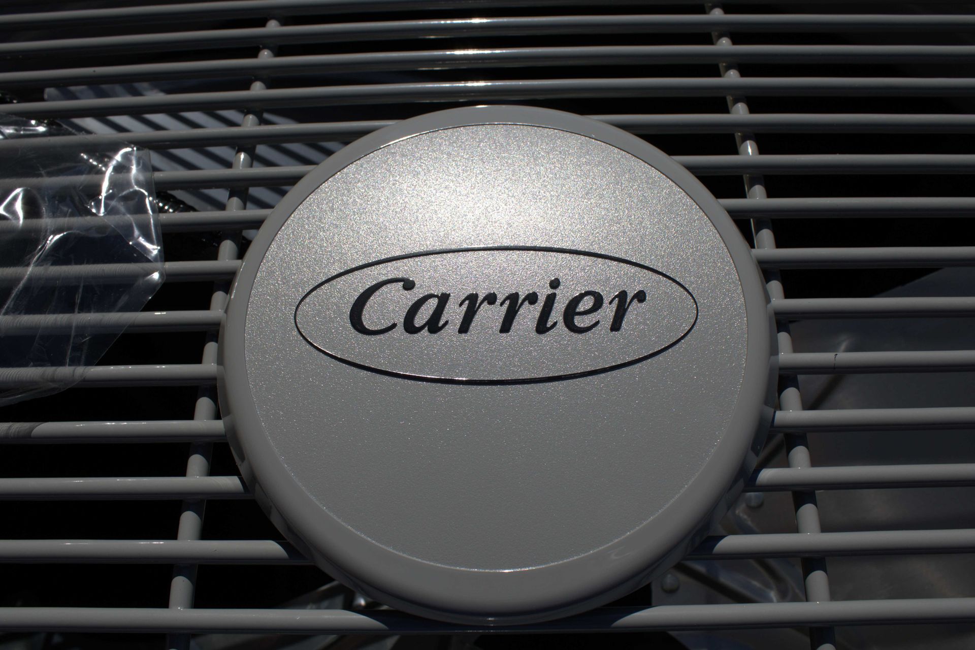 Close-up of a Carrier air conditioner logo on a gray, circular cover within a metal grate.