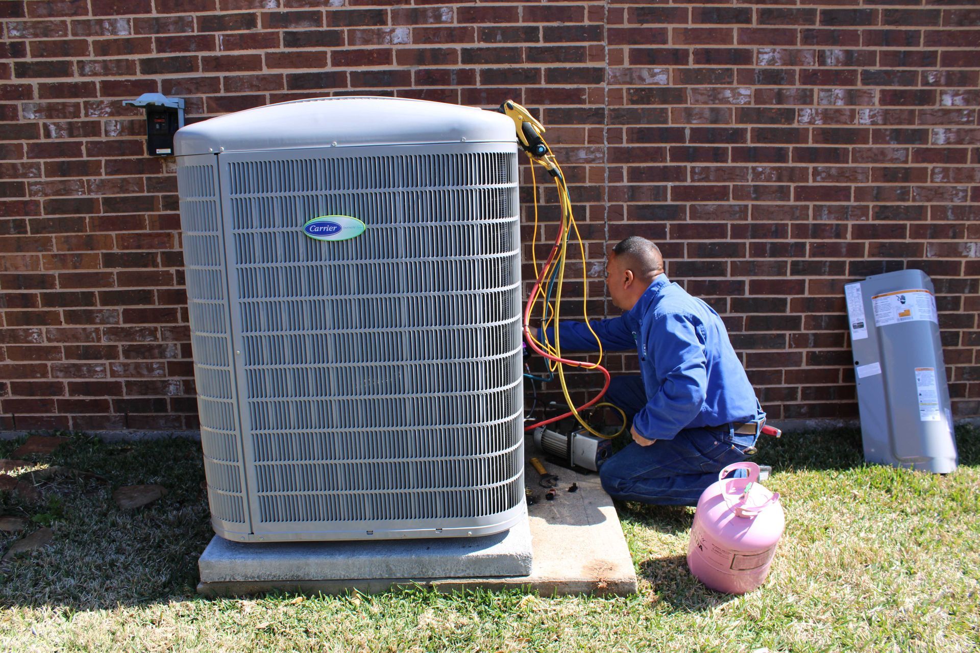HVAC technician servicing an air conditioning unit outside a brick building.