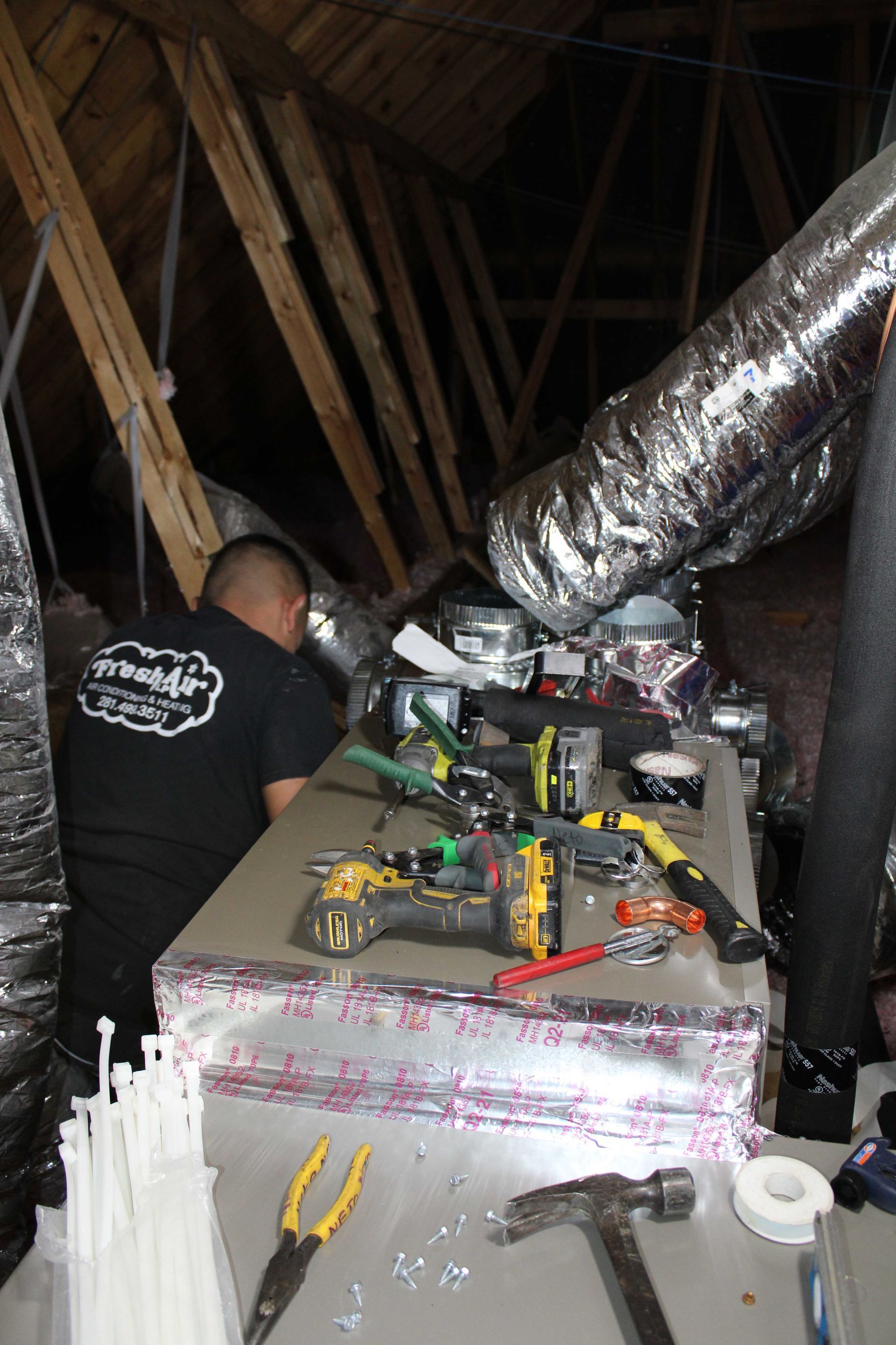 HVAC technician working in an attic, surrounded by tools and ductwork.
