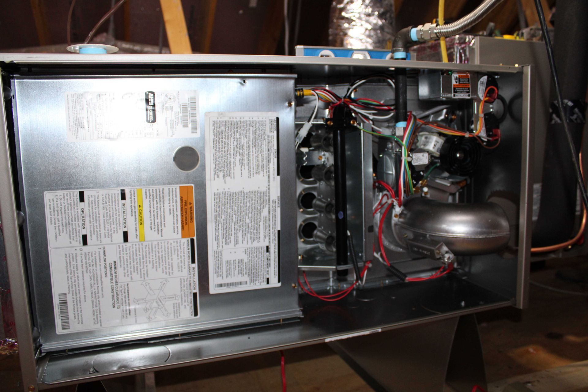 Furnace unit with open panel, showing internal components and wiring in an attic setting.