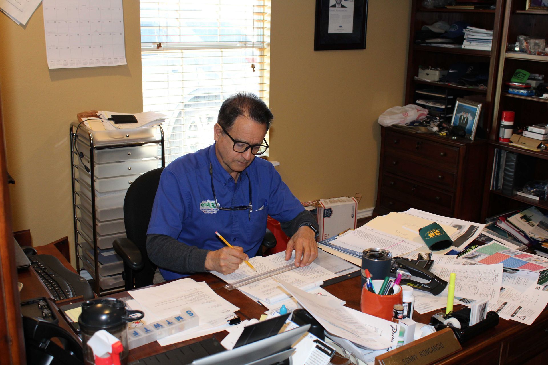 Man in glasses working at a cluttered desk in an office.