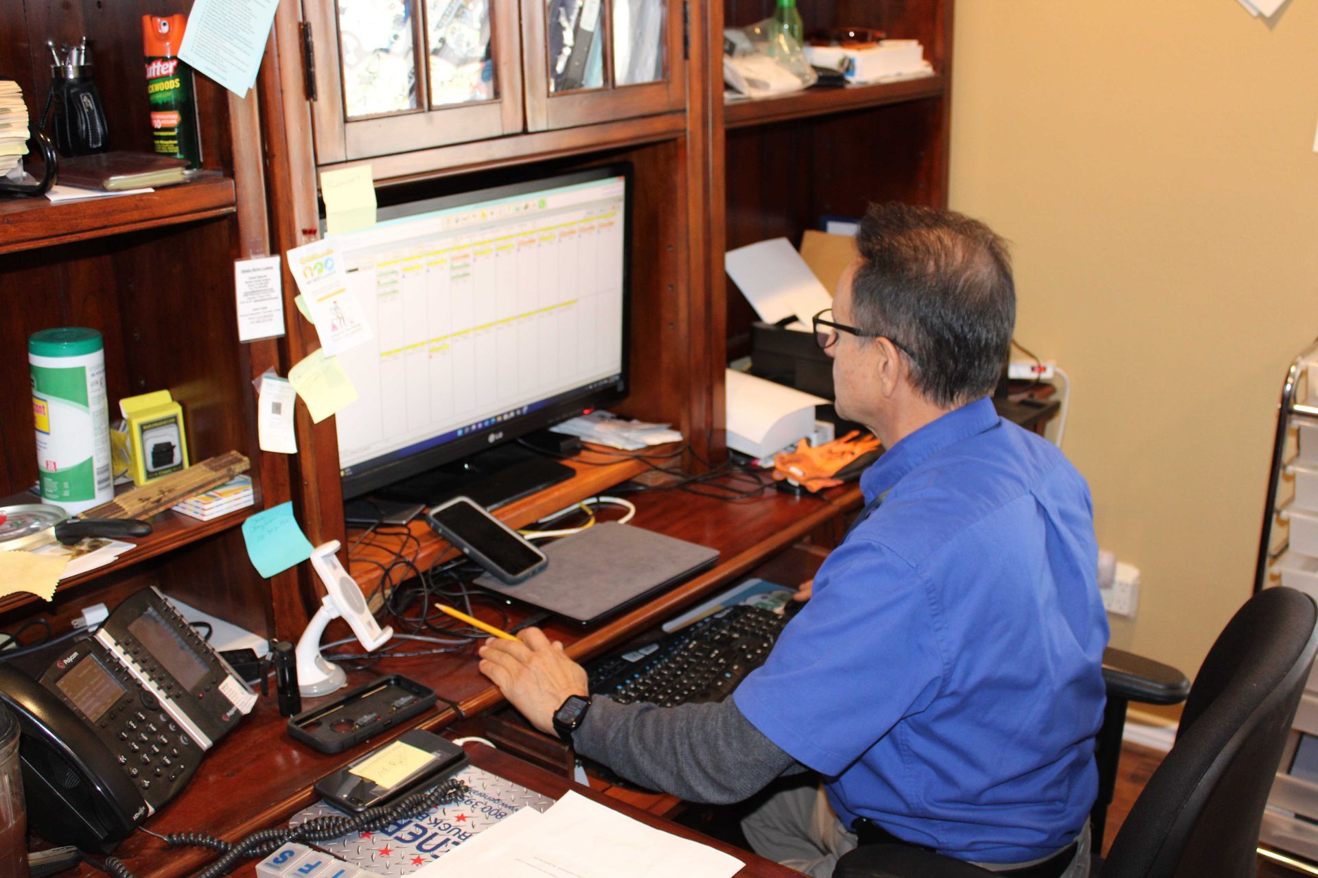 Man sitting at a desk, typing on a computer, looking at the screen. Brown desk, blue shirt.