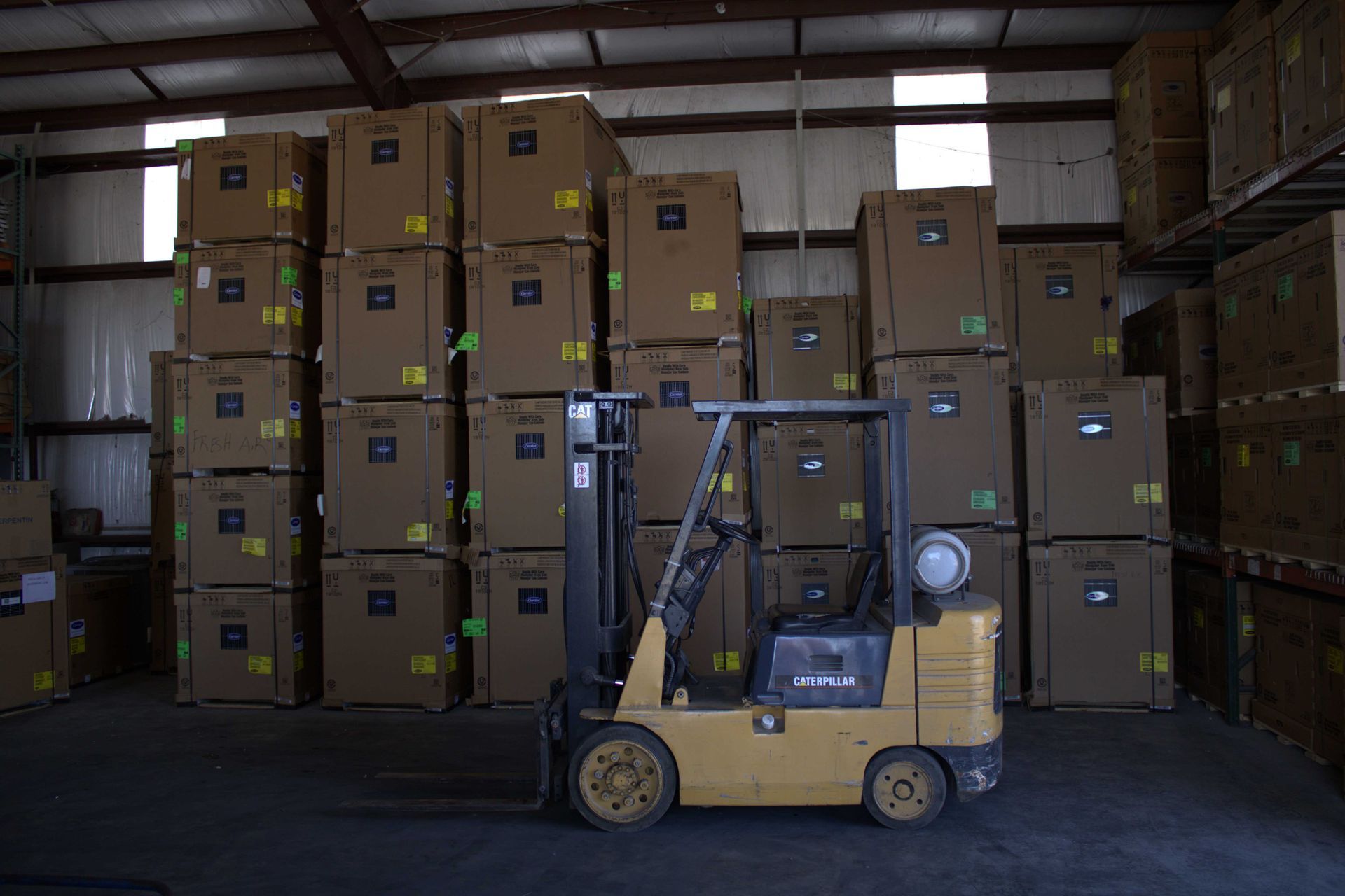 Yellow forklift in a warehouse, boxes stacked high, some on shelves.