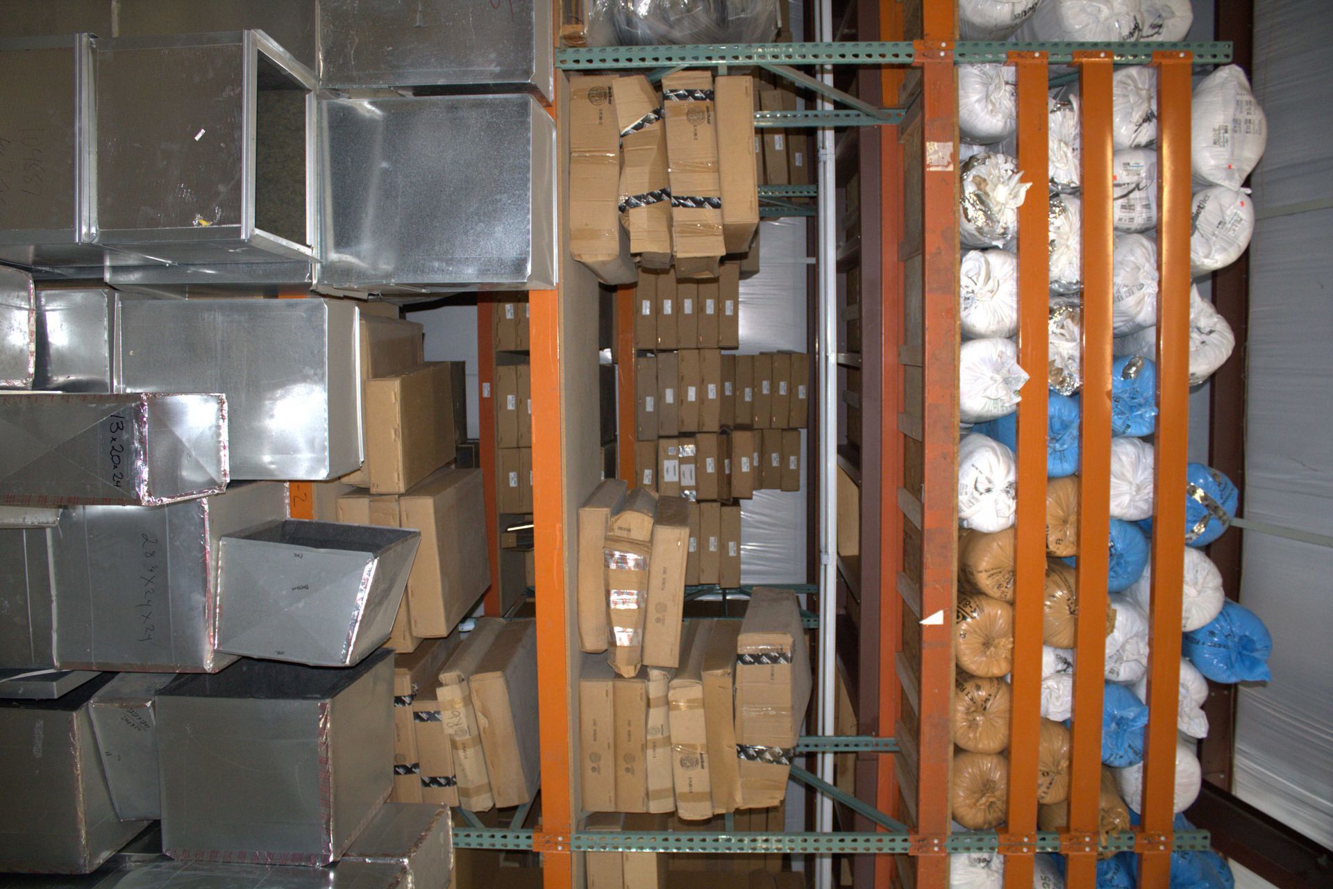 Shelves stacked with various boxes and rolls of fabric in a warehouse setting.