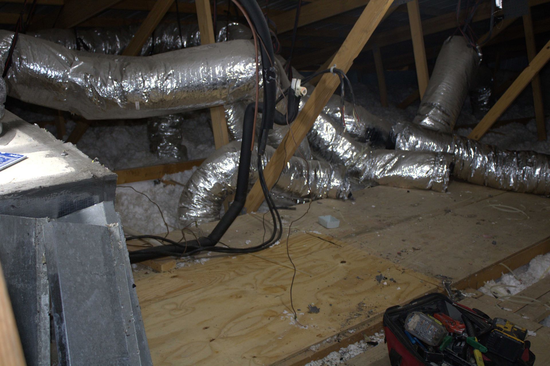 Attic with ductwork and a wooden floor; wires and a toolbox present.