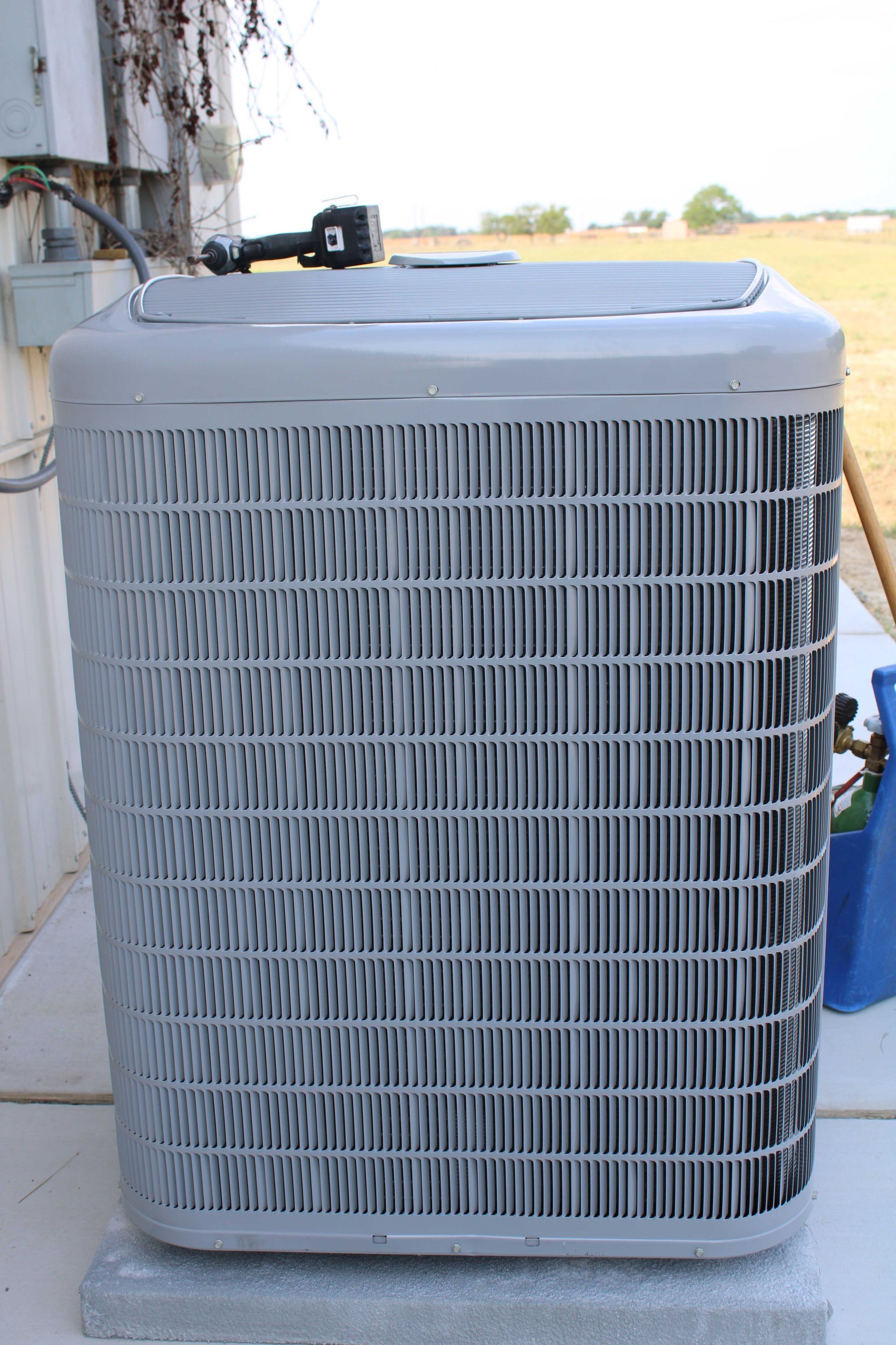 Gray air conditioning unit on a concrete block, outdoors.