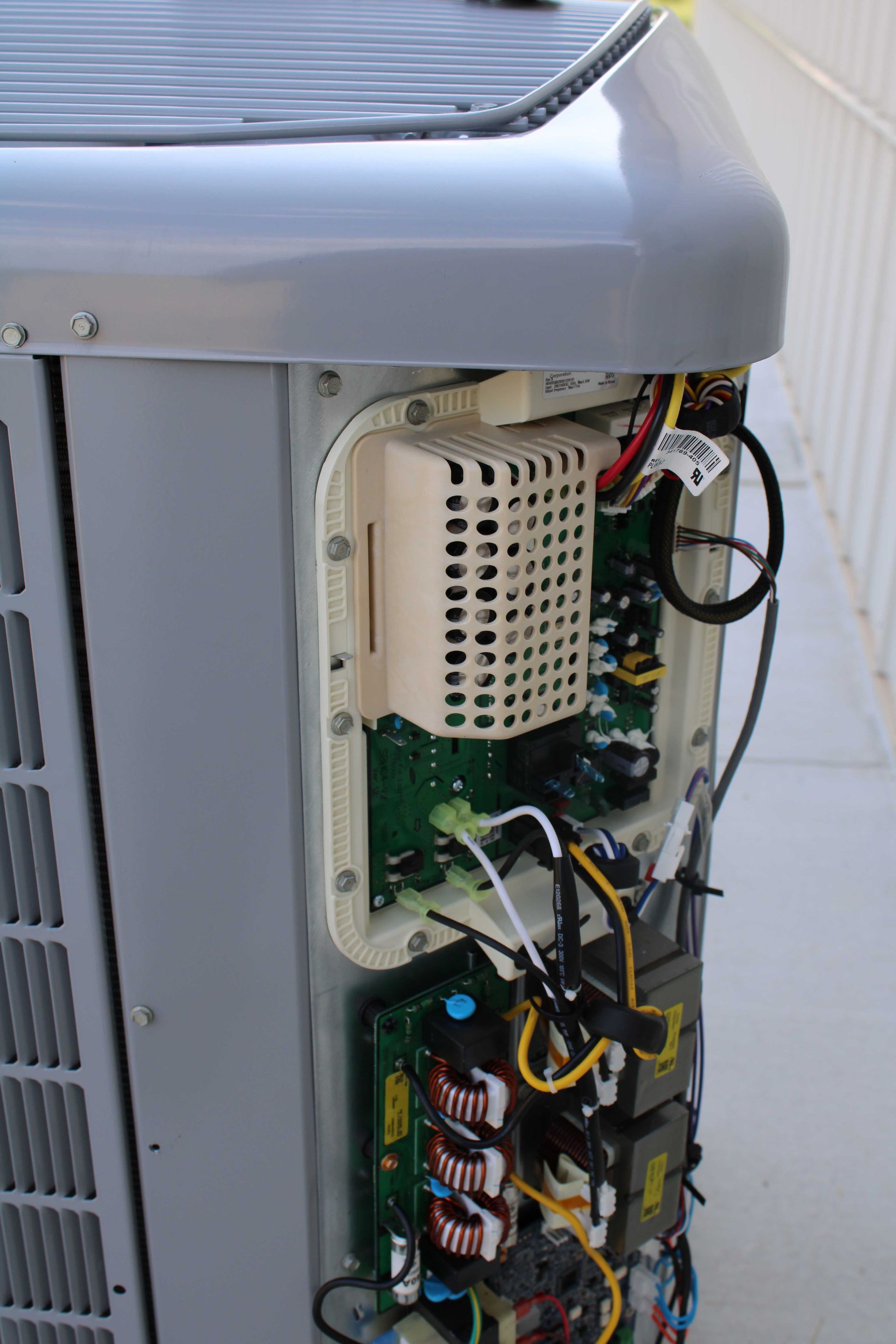 Side view of an AC unit with an open access panel revealing internal circuit boards and wiring.