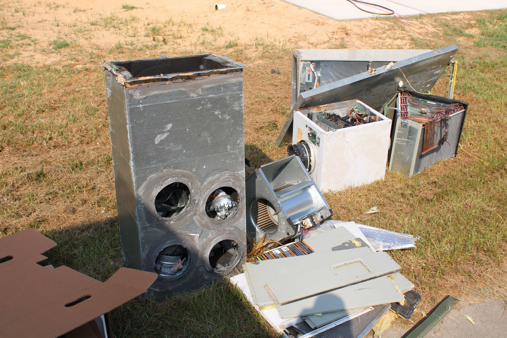 Scrap metal and parts from an HVAC system scattered on grass in daylight.
