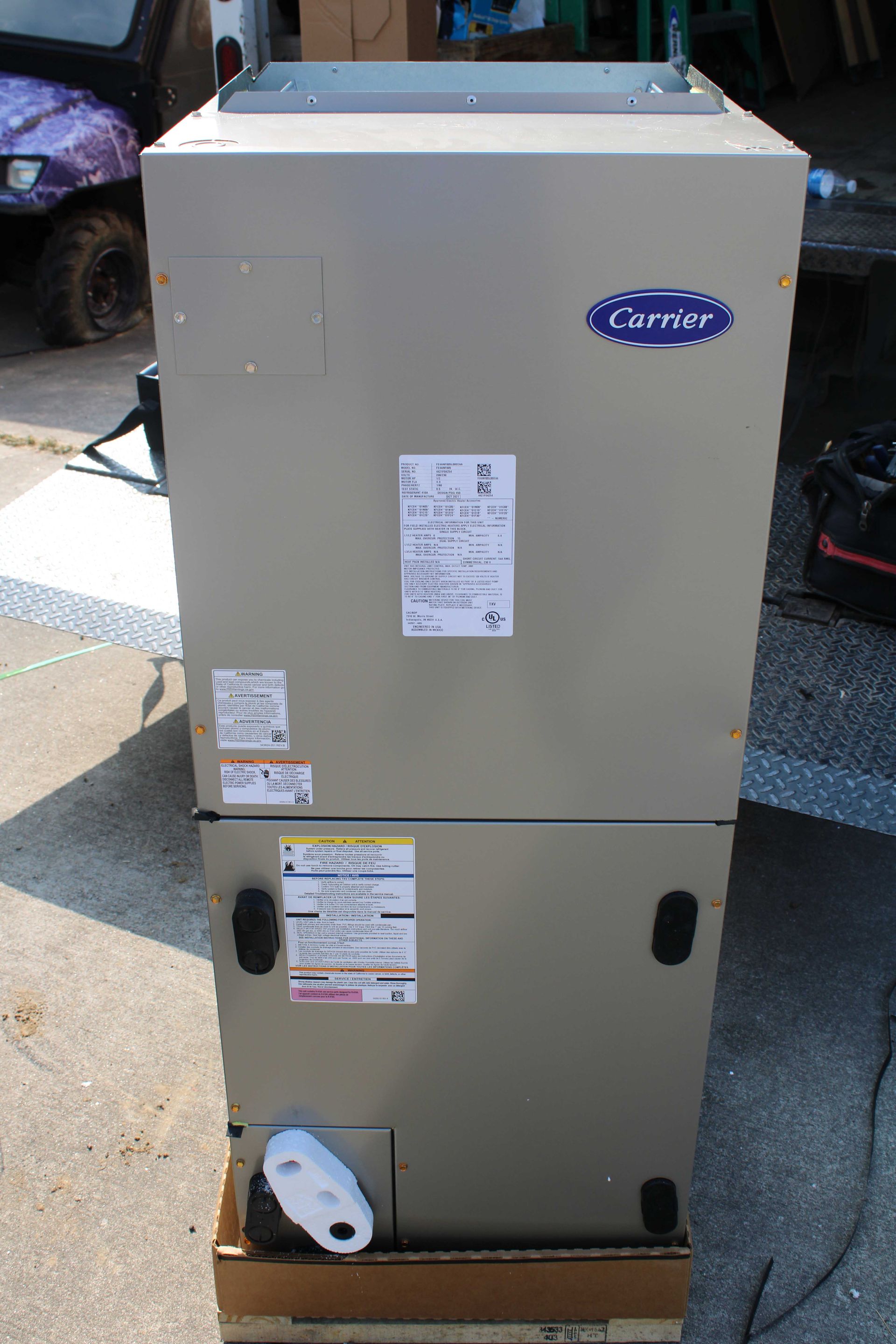 Carrier HVAC unit, tan, standing outdoors on cardboard, with labels and access panels.