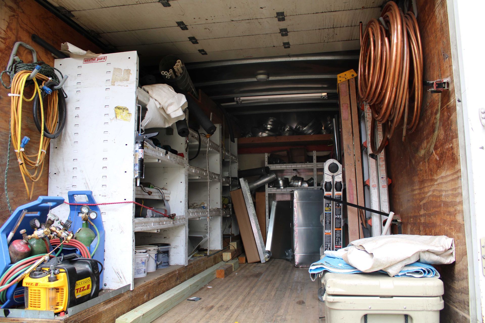 Inside of a work truck filled with tools and equipment, including tanks, shelves, and copper tubing.