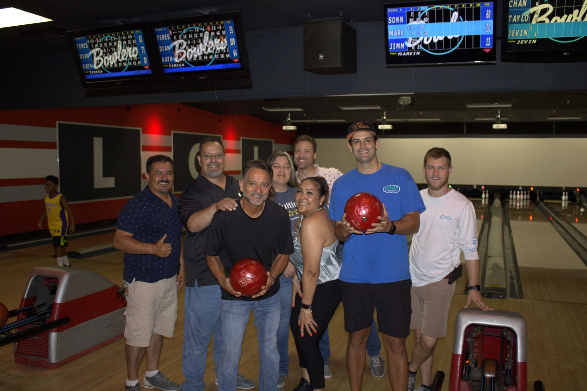 Group of people holding bowling balls in a bowling alley.