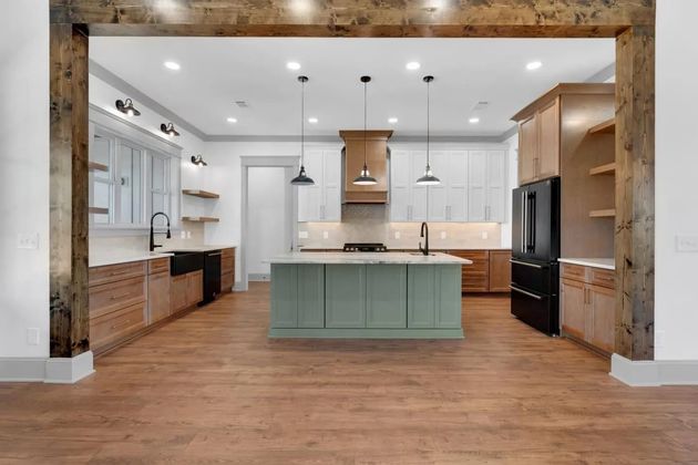 Bright modern kitchen with white cabinets, wood floors, and a mint-green island beneath exposed beams