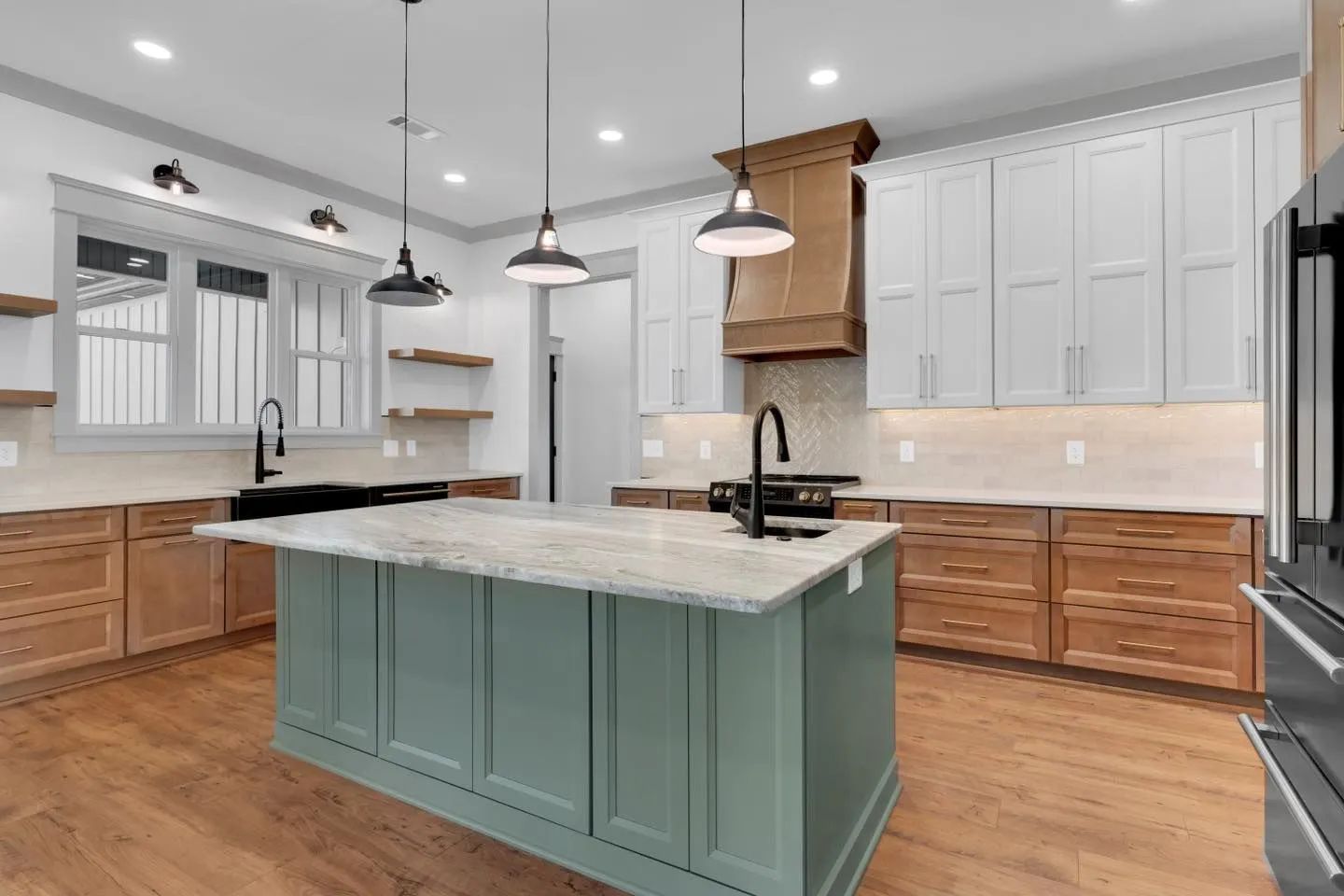 Modern kitchen with teal island, white cabinets, wood accents, and pendant lights