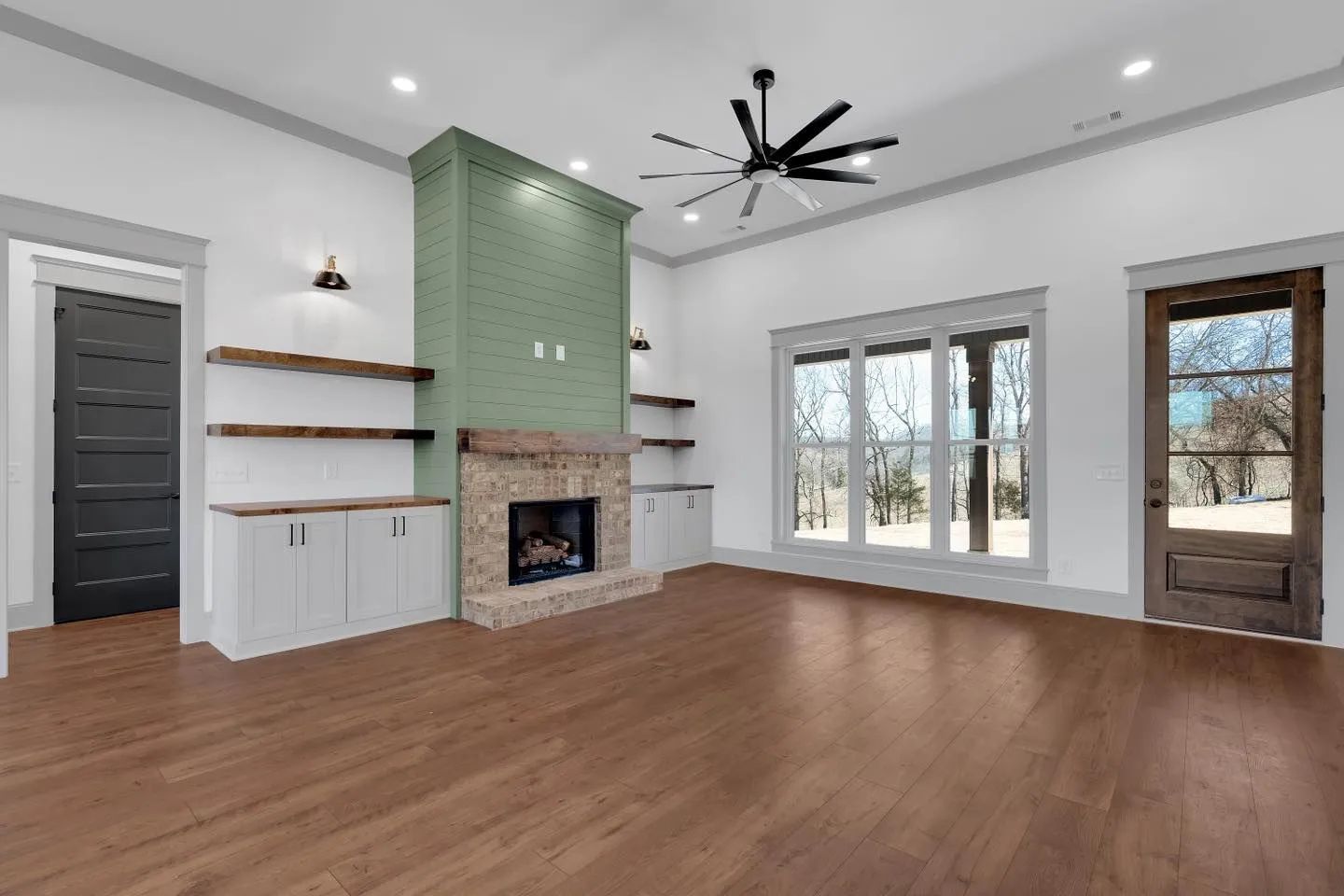 Bright living room with green fireplace, hardwood floors, large windows, and a door to the outside.