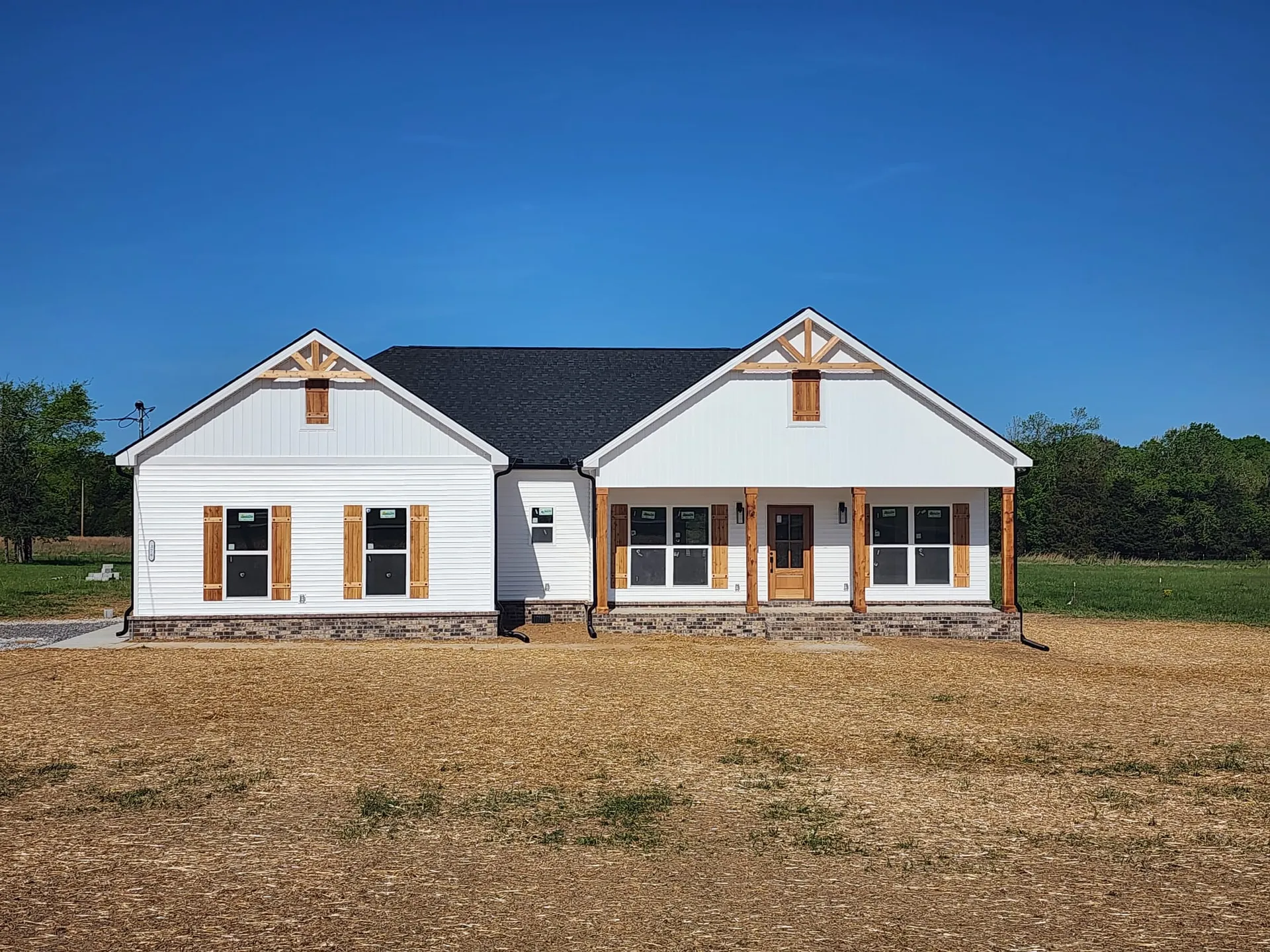 New white house with black roof and porch in a grassy field under a clear blue sky