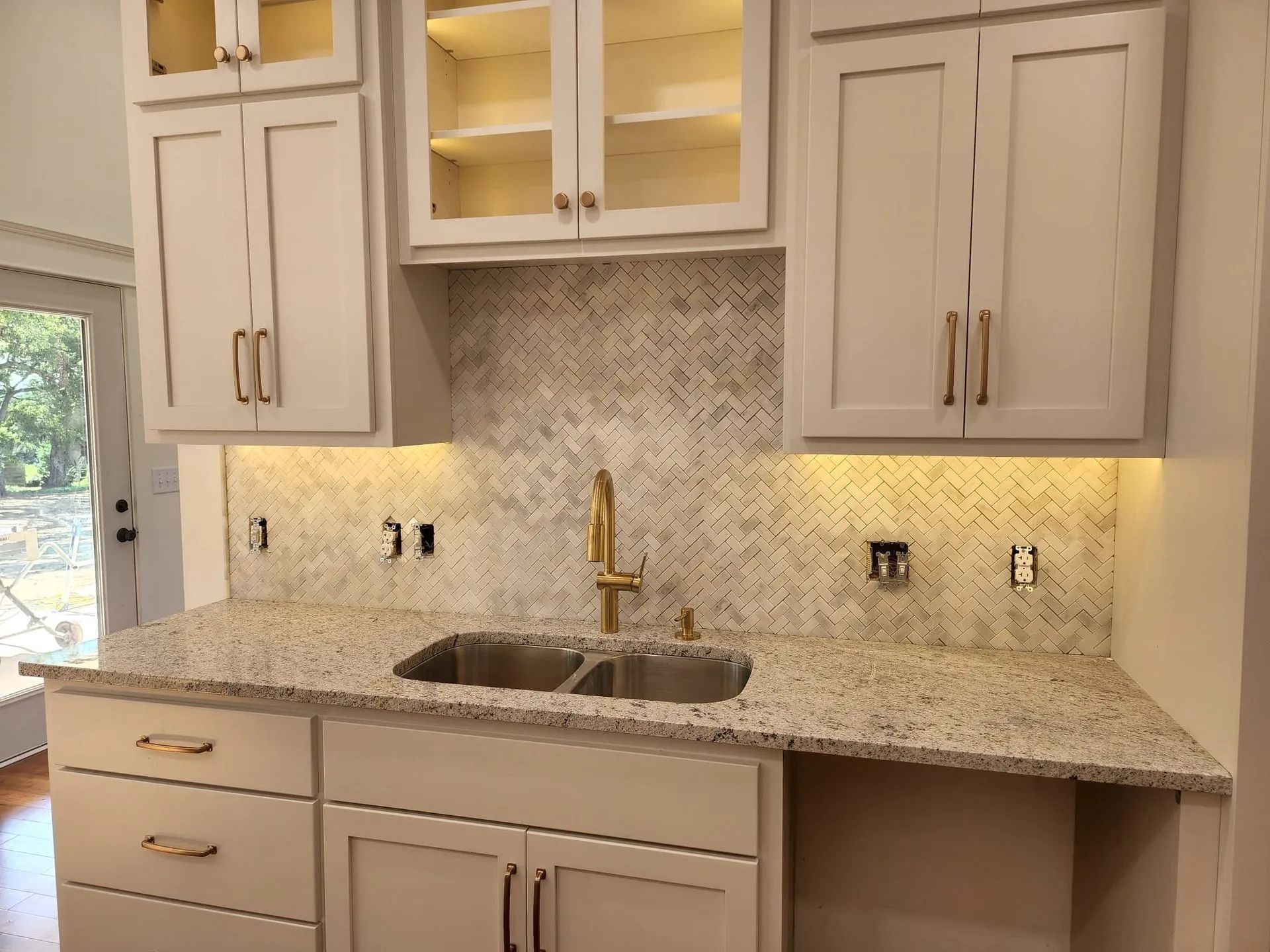 Modern kitchen with light wood cabinets, granite countertop, and mosaic tile backsplash under warm under-cabinet lighting