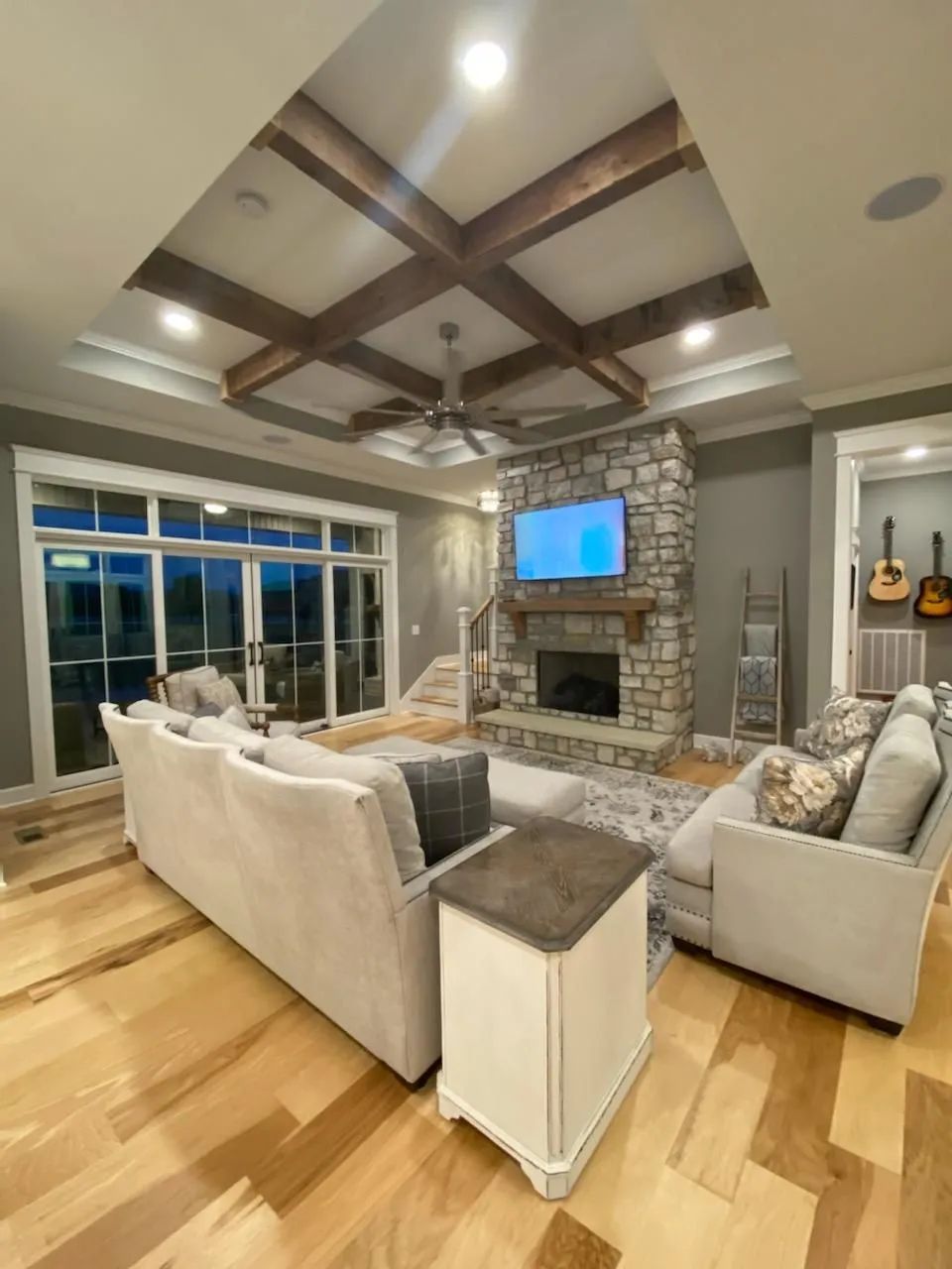 Spacious living room with beige sofas, stone fireplace, wood-beam ceiling, and large windows