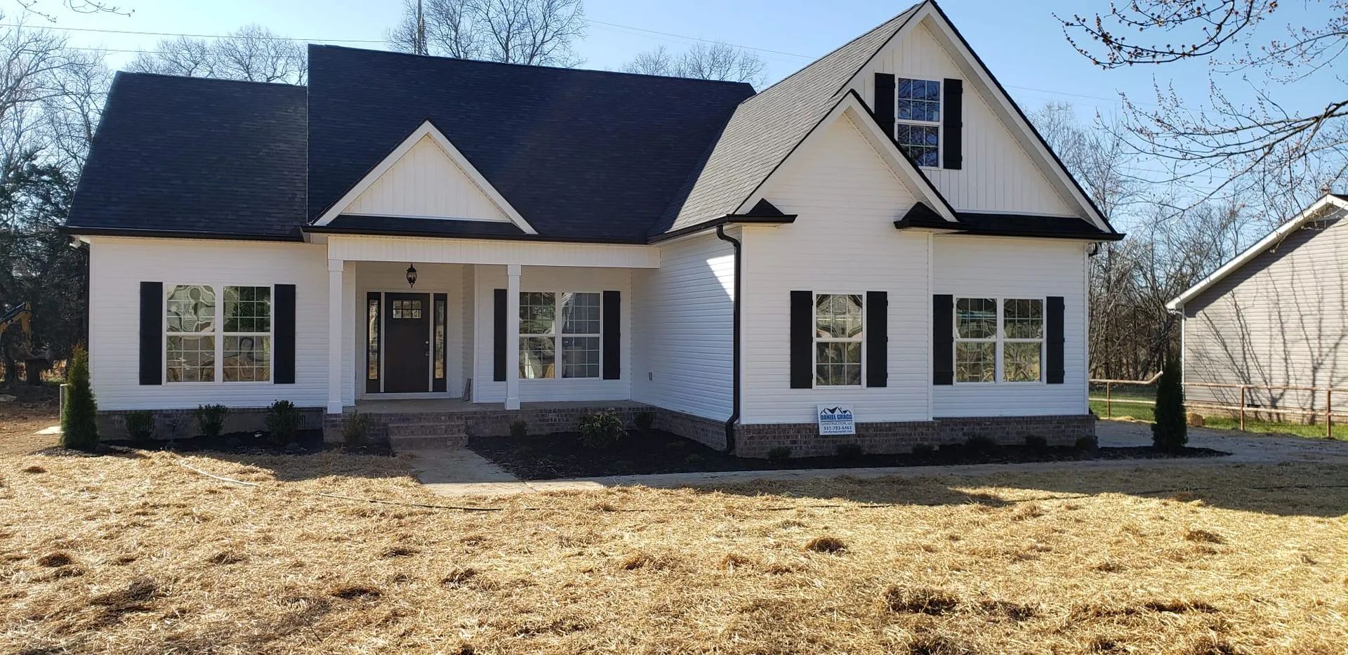 White house with dark roof and front porch in a grassy yard on a sunny day