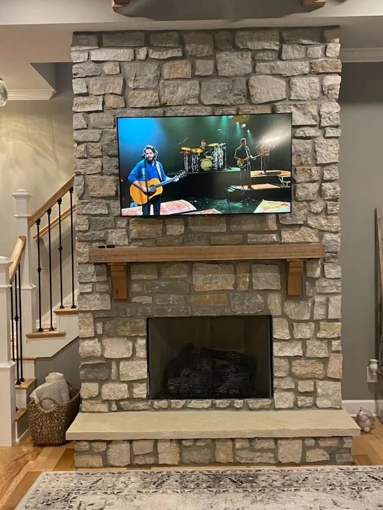 Stone fireplace with mounted TV, wooden mantel, and stairway beside it in a living room