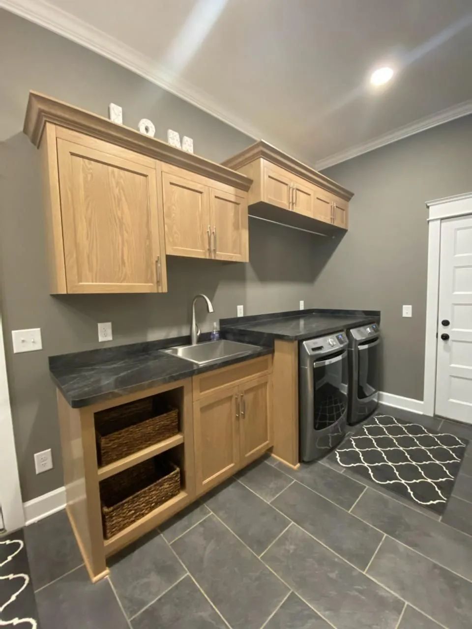 Modern kitchen with light wood cabinets, dark countertops, gray tile floor, and black appliances