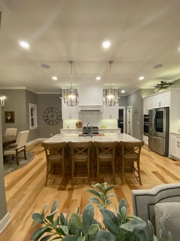 Bright open kitchen with island, wooden barstools, stainless appliances, and pendant lights over hardwood floors