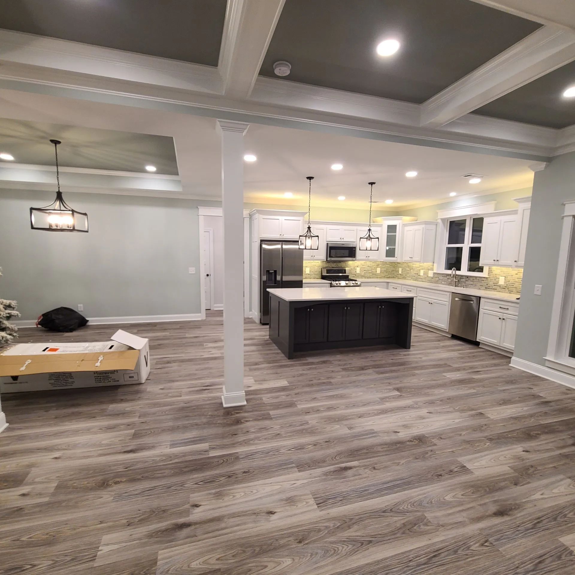 Spacious modern open-concept kitchen and living room with gray floors, white columns, and pendant lights.