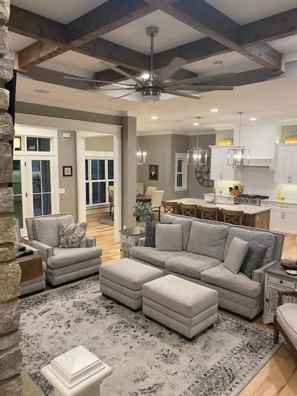 Bright living room with gray sofa, patterned rug, tray ceiling, and open kitchen in the background