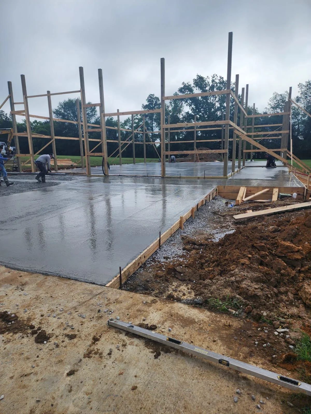 Concrete slab under construction with wooden framing and wet surface on a cloudy day