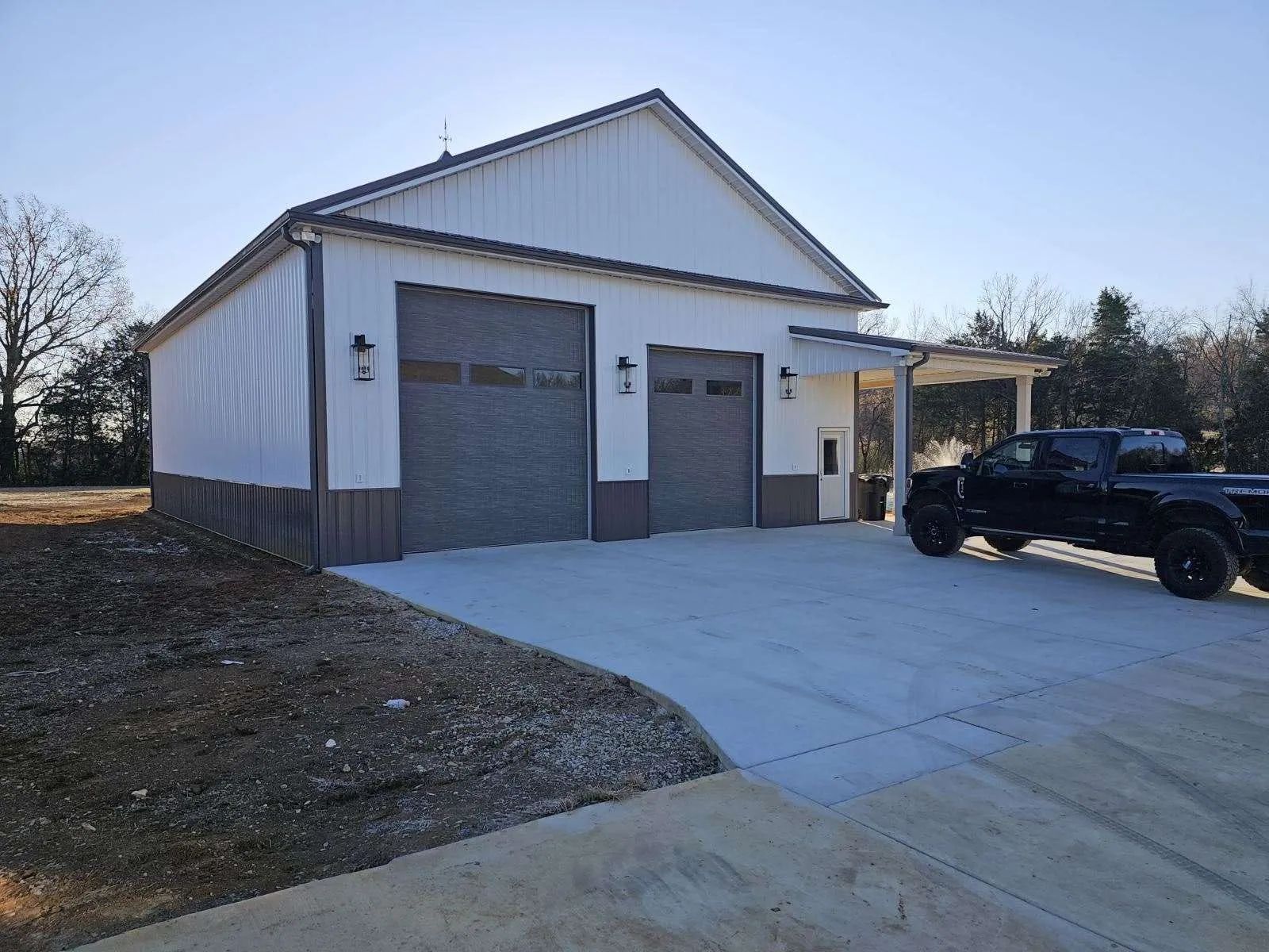 Metal garage with white siding and two gray doors beside a driveway, with a black SUV parked outside.