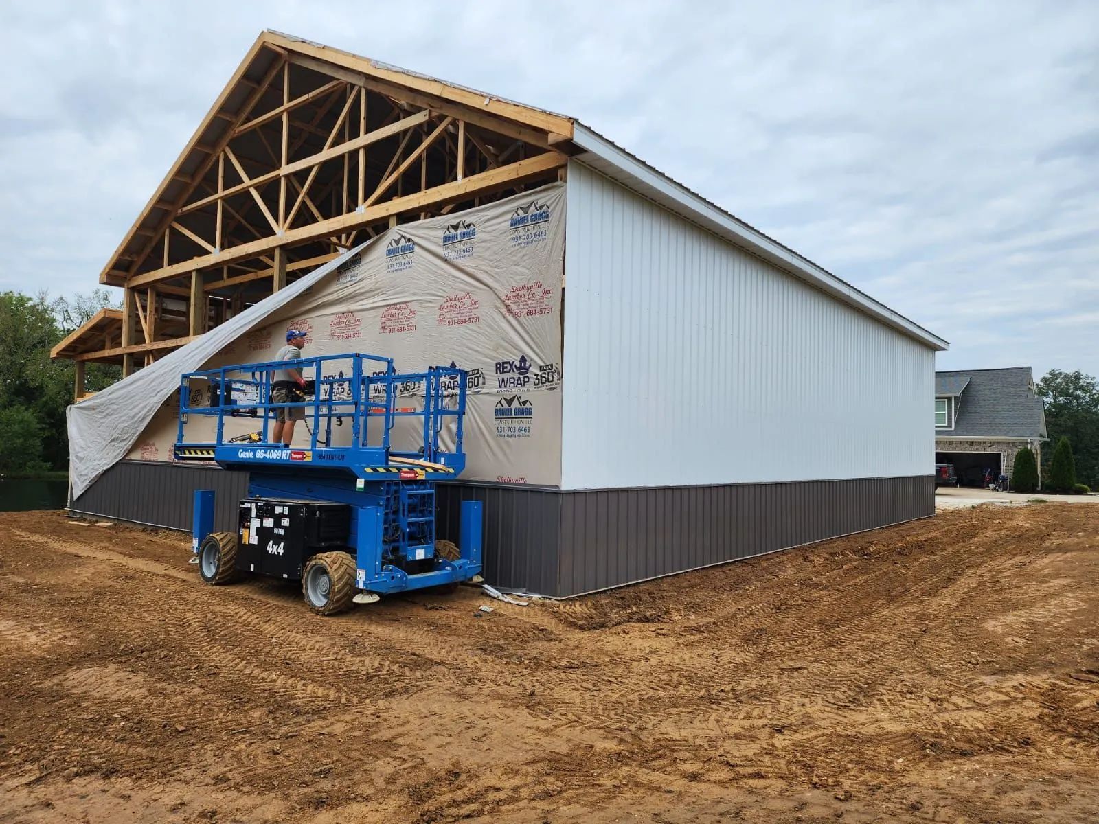 Construction site with a barn under construction and a blue lift on dirt ground