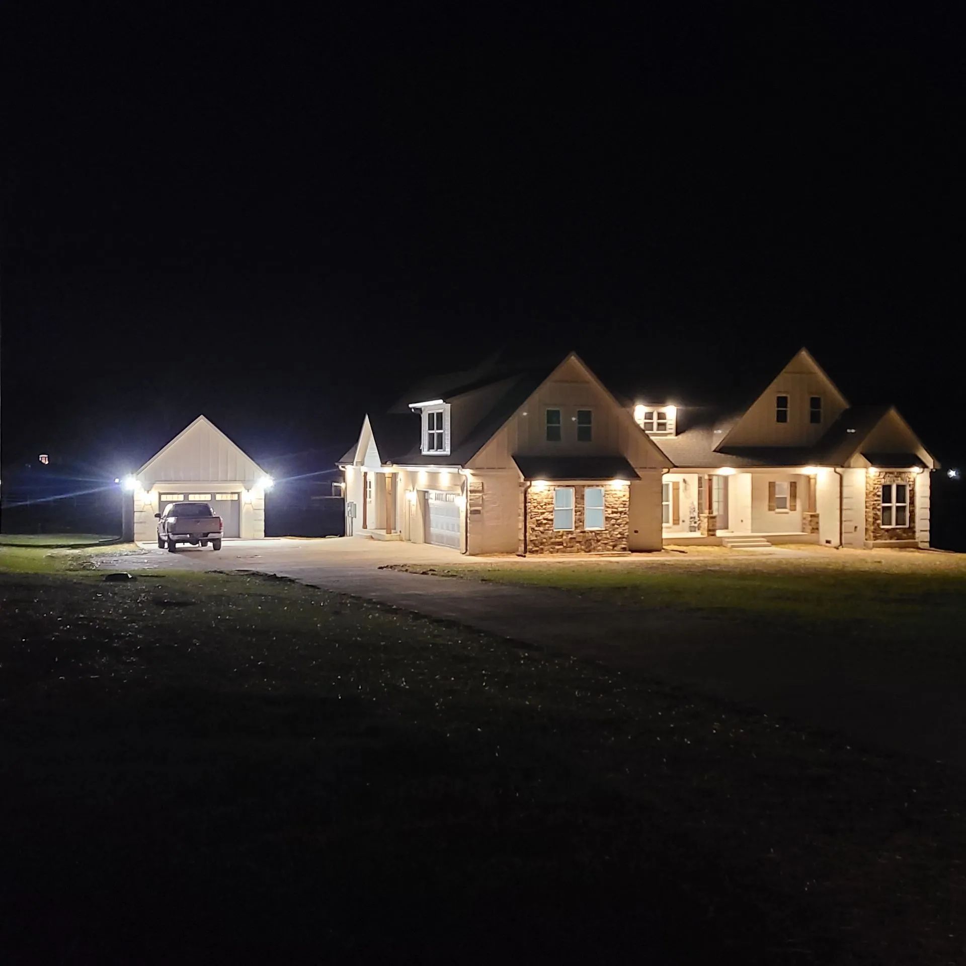Illuminated house at night with a garage and car on a dark lawn