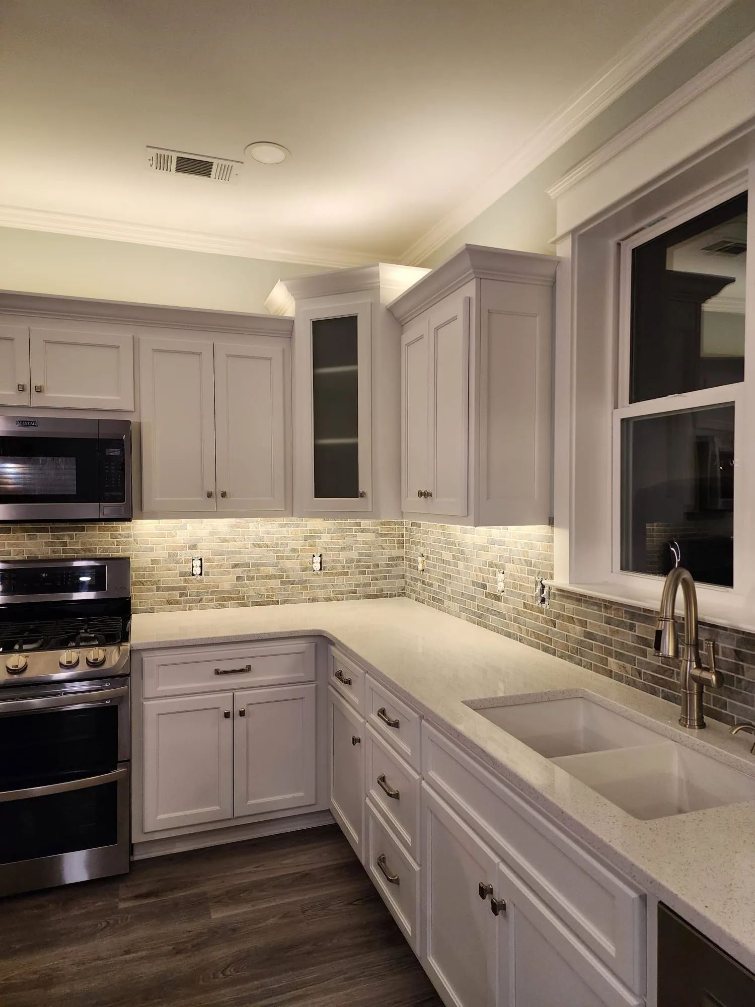 Modern white kitchen with gray cabinets, marble countertops, subway tile backsplash, and a double sink by the window
