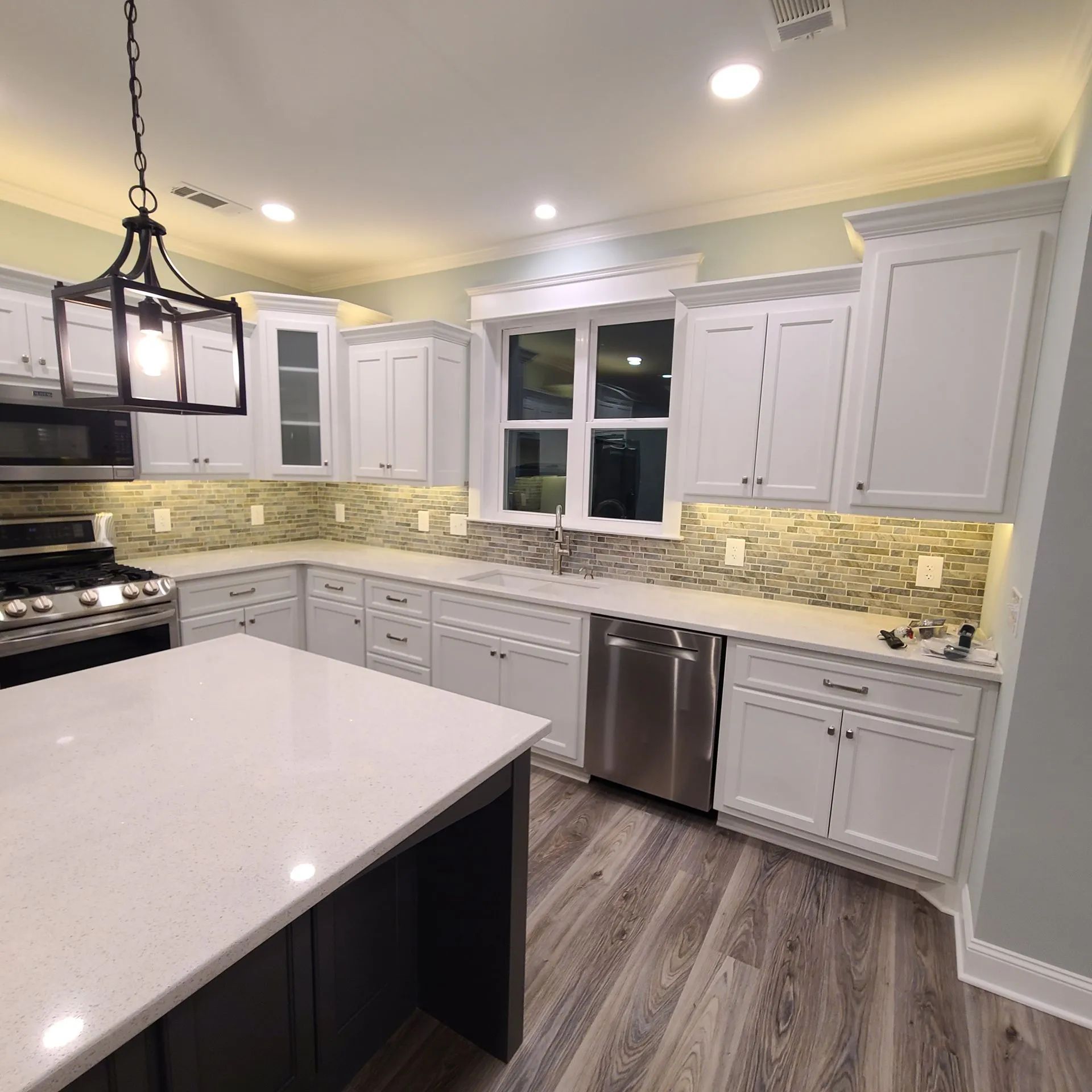 Bright modern kitchen with white cabinets, island, stainless appliances, and mosaic backsplash