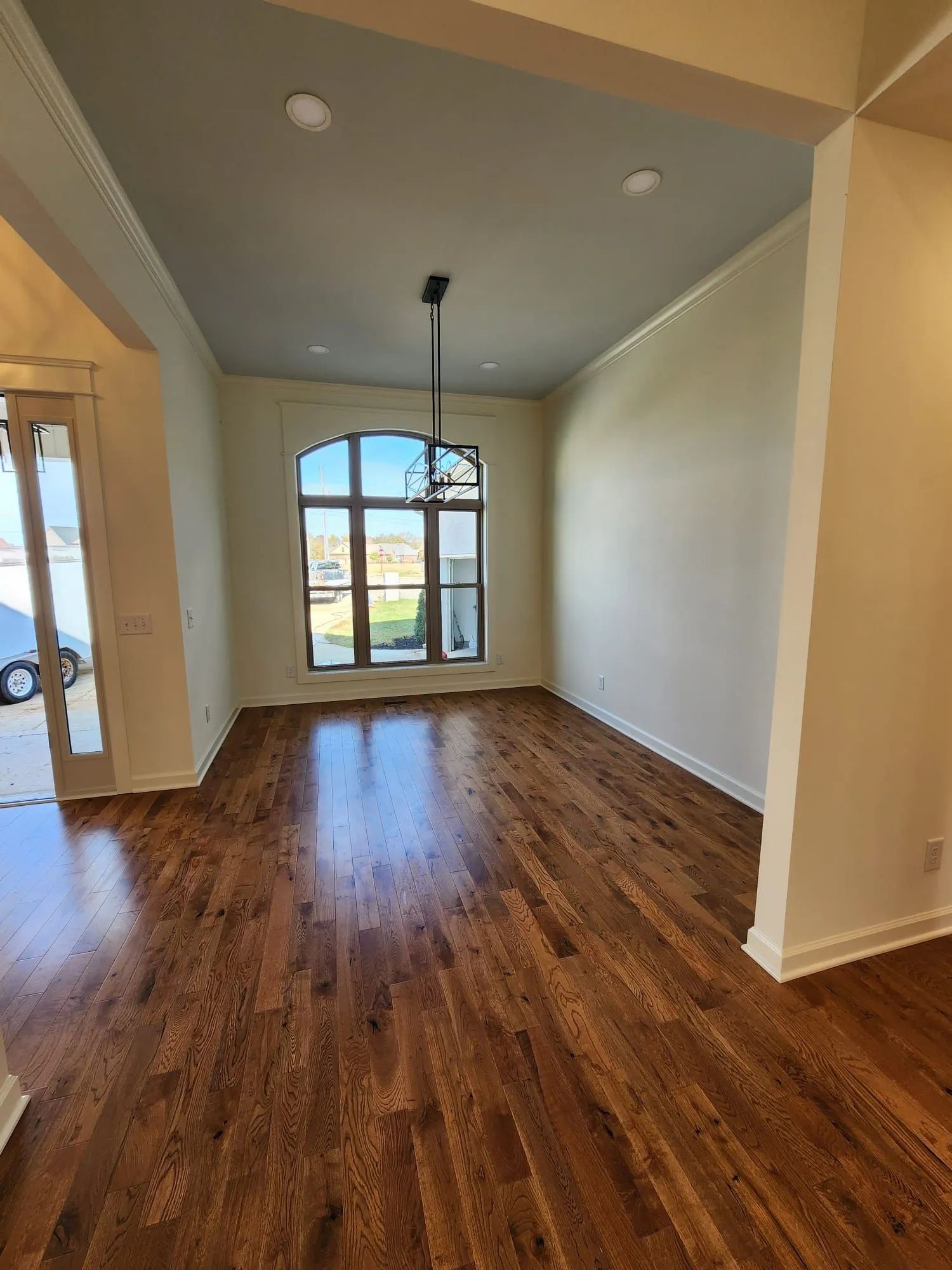Empty beige living room with hardwood floors and a large arched front window.