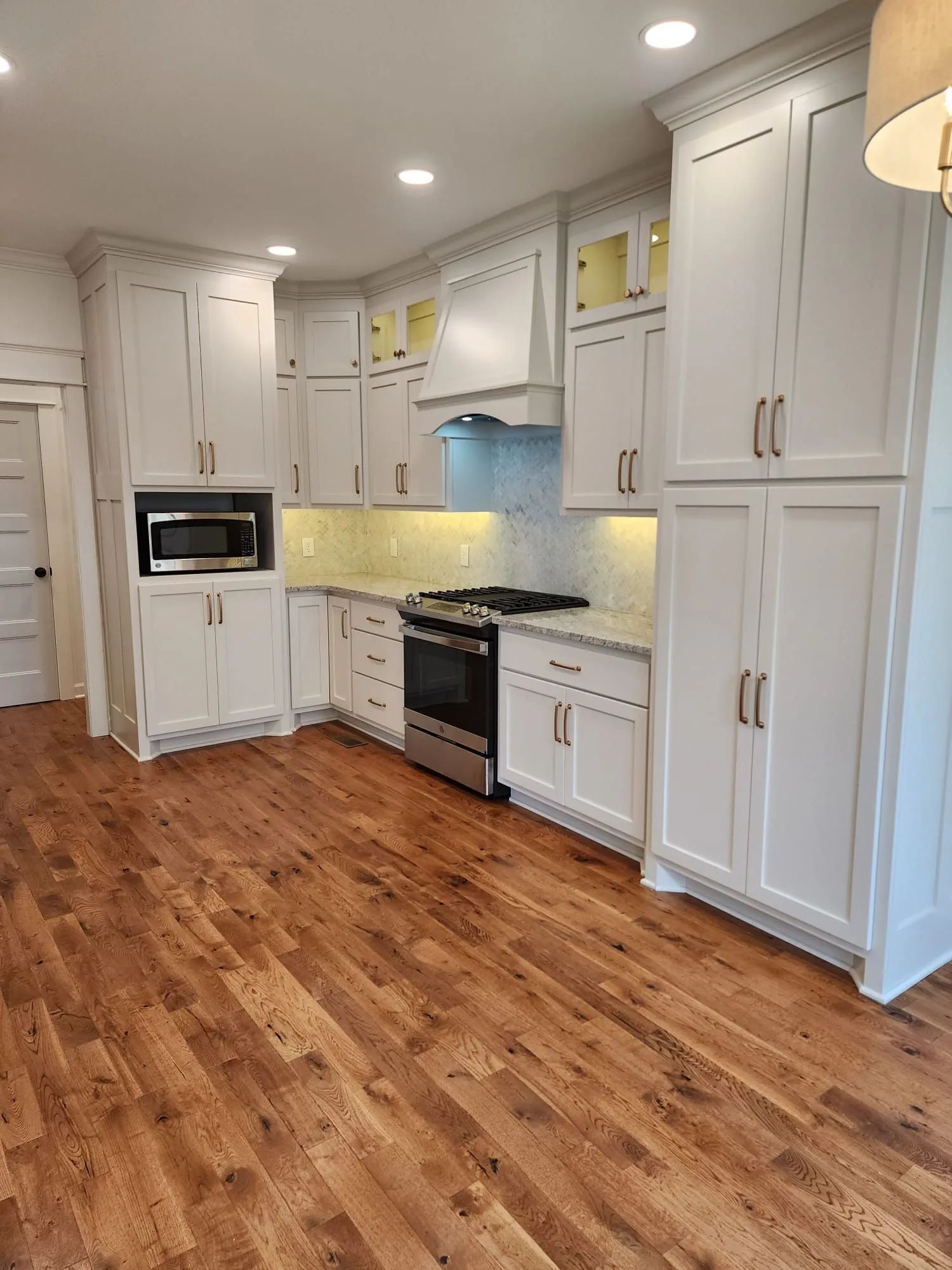Bright modern kitchen with white cabinets, stainless stove, and warm wood floors