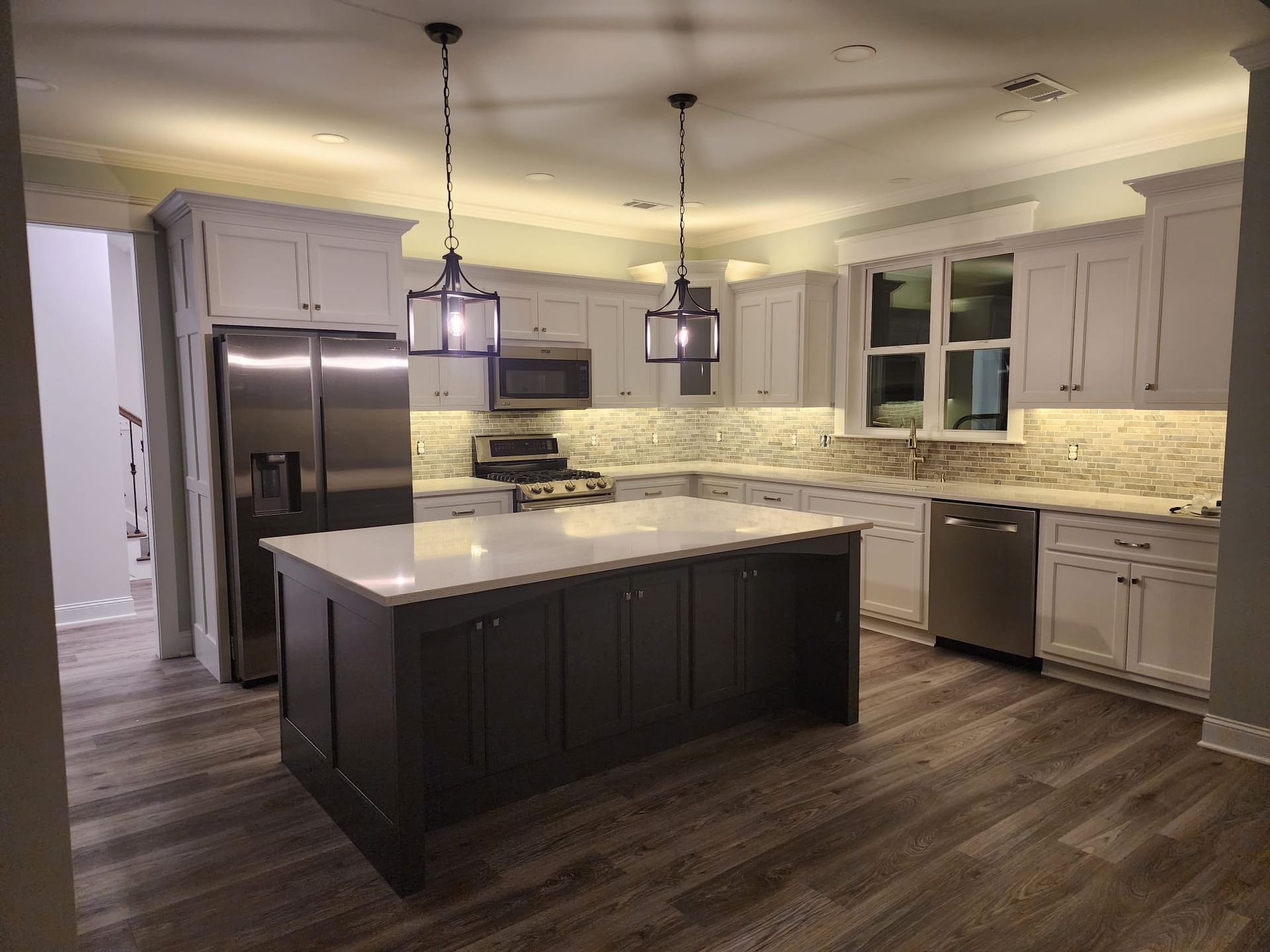 Modern kitchen with dark island, stainless steel appliances, gray cabinets, and under-cabinet lighting