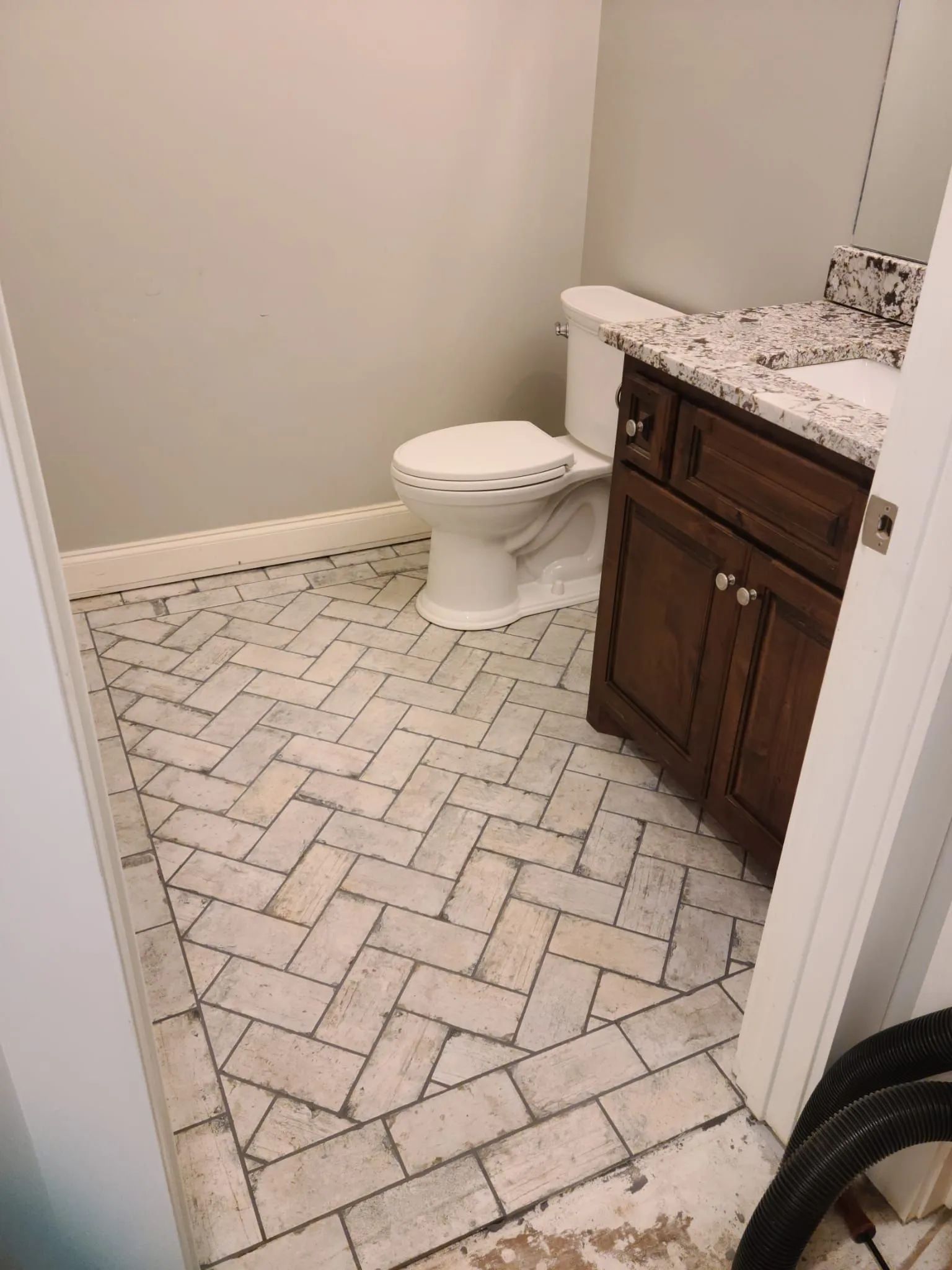 Small bathroom with white tile floor, toilet, and dark wood vanity with granite countertop.