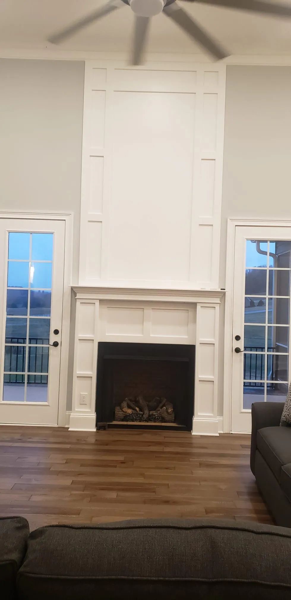 Living room with a tall white fireplace flanked by windows and hardwood floors