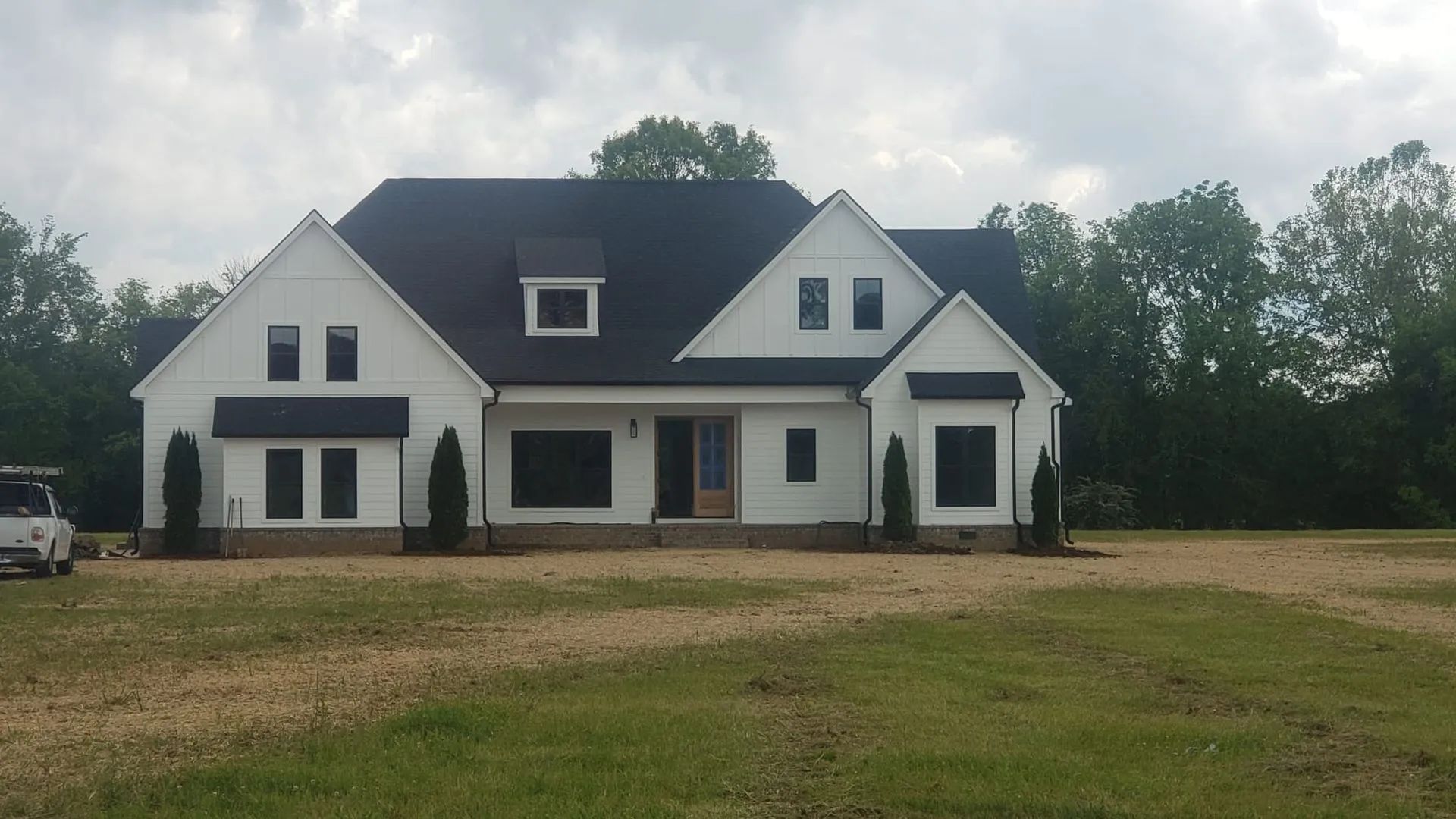 Large white house with a dark roof and dormer windows on a grassy lot, viewed from the front
