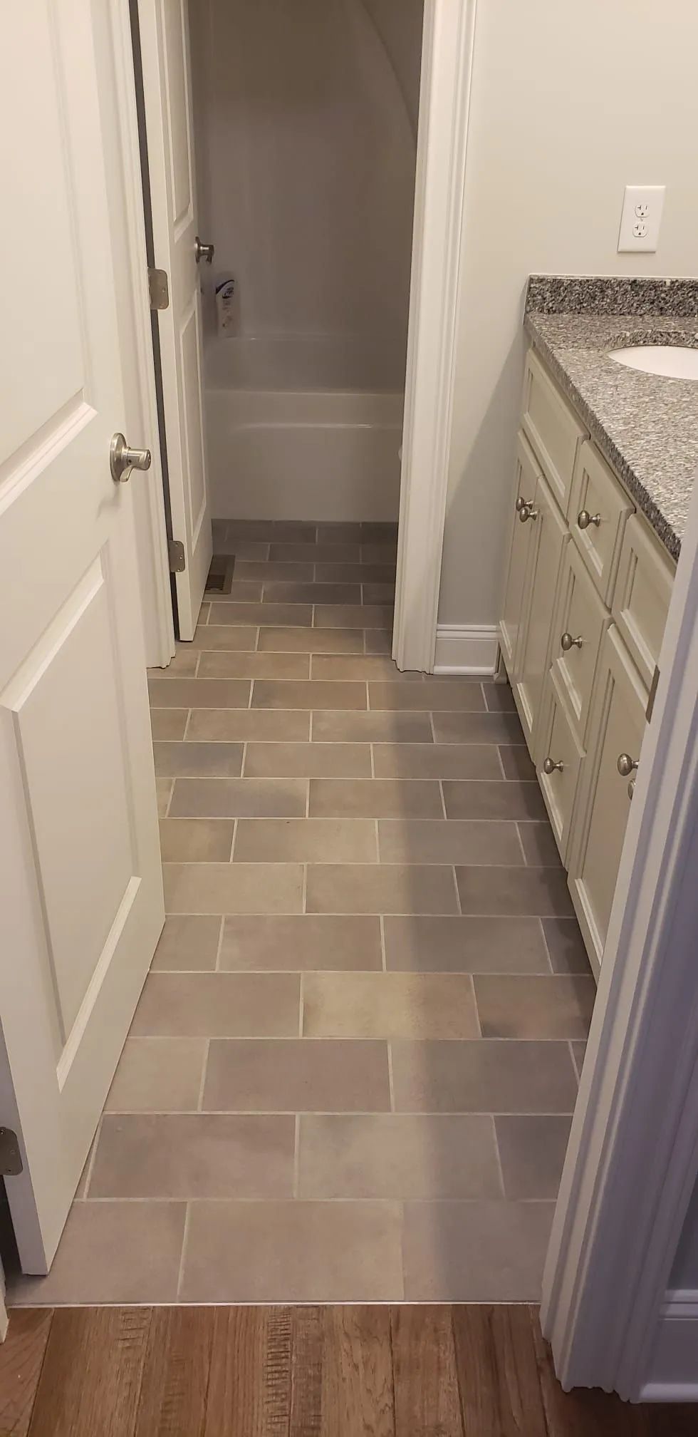 Narrow bathroom hallway with gray tile floor, vanity on the right, and a doorway to a closet or shower.
