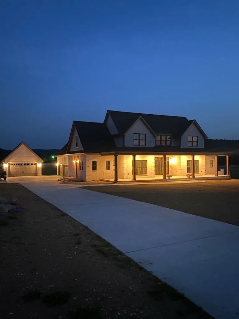 Large house at dusk with warm porch lights and a driveway under a dark blue sky.