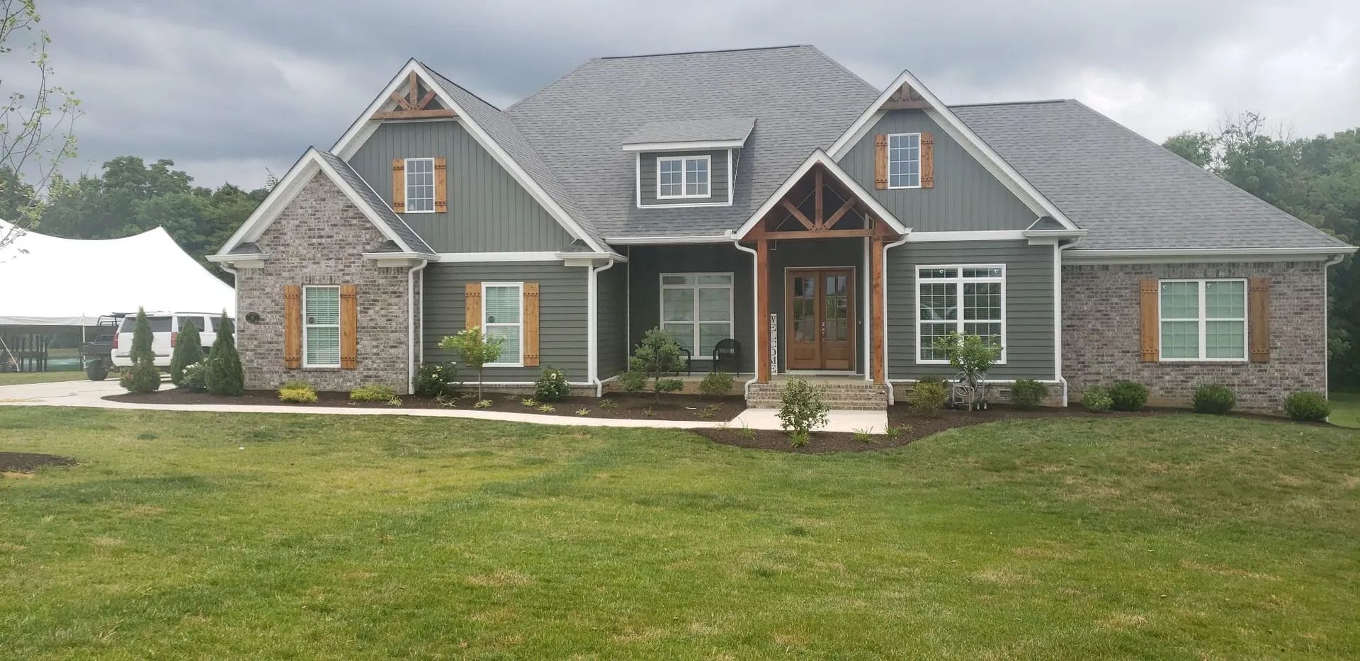 Stone-and-brick suburban house with gray roof and large front lawn under an overcast sky