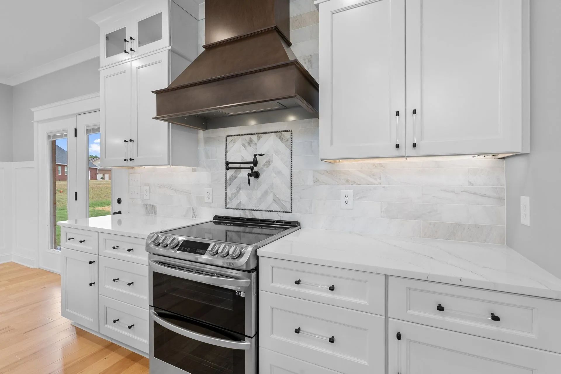 White kitchen with stainless steel stove, dark hood, marble backsplash, and built-in cabinets